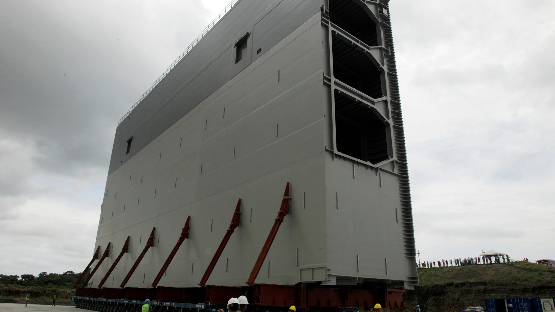 FILE - In this Aug. 22. 2013 file photo, a section of the new rolling gates for the Panama Canal's third set of locks towers over workers during a press tour in Gatun, Panama. The consortium carrying out a historic expansion of the Panama Canal says it may have to suspend work due to financial problems caused by a $1.6 billion cost overrun. The group issued a statement Wednesday, Jan. 1, 2014, giving the Panama Canal Authority 21 days to settle the dispute, but says it will continue working in the meantime. (AP Photo/Arnulfo Franco, File)