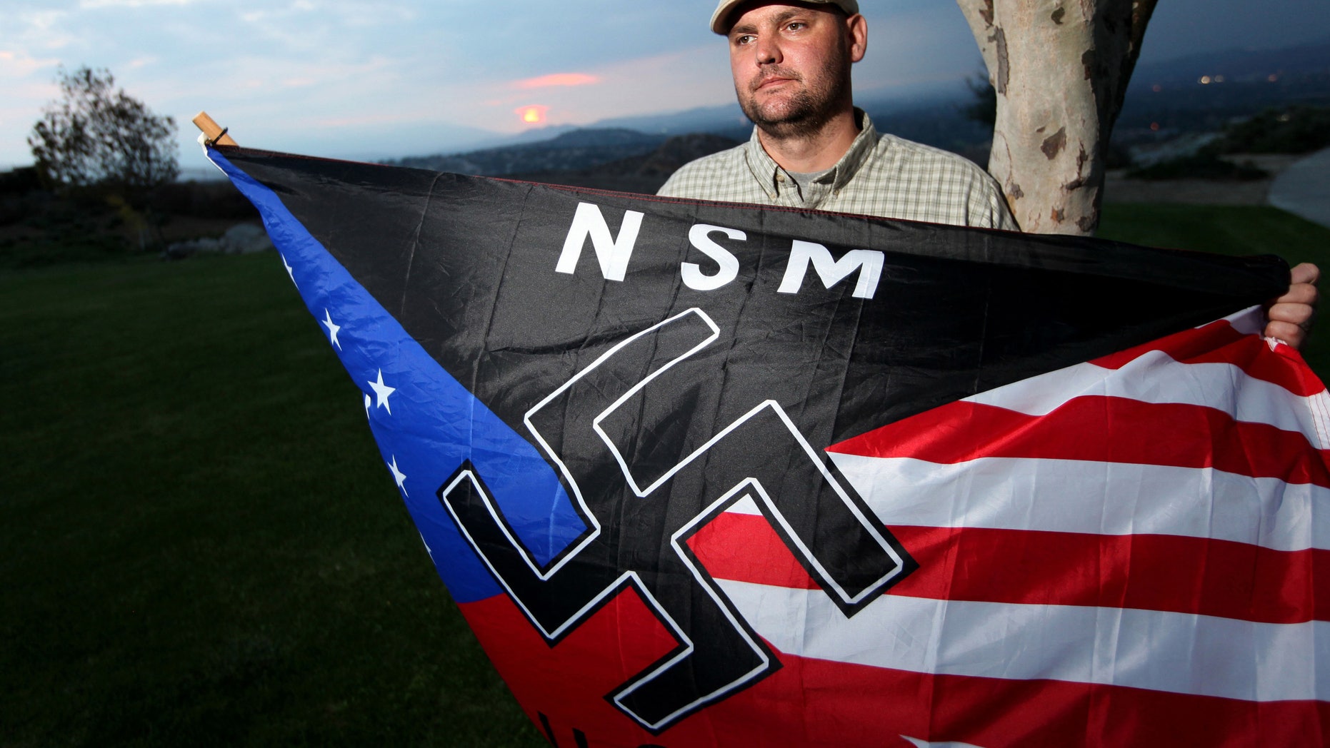 FILE - In this Oct. 22, 2010 file photo, Jeff Hall, who was killed by his son, holds a Neo Nazi flag while standing at Sycamore Highlands Park near his home in Riverside, Calif. Defense attorneys for a boy charged with killing Hall, his neo-Nazi father when he was 10 years old has rested its case without calling the boy to testify, Wednesday, Jan. 9, 2013. (AP Photo/Sandy Huffaker, File)