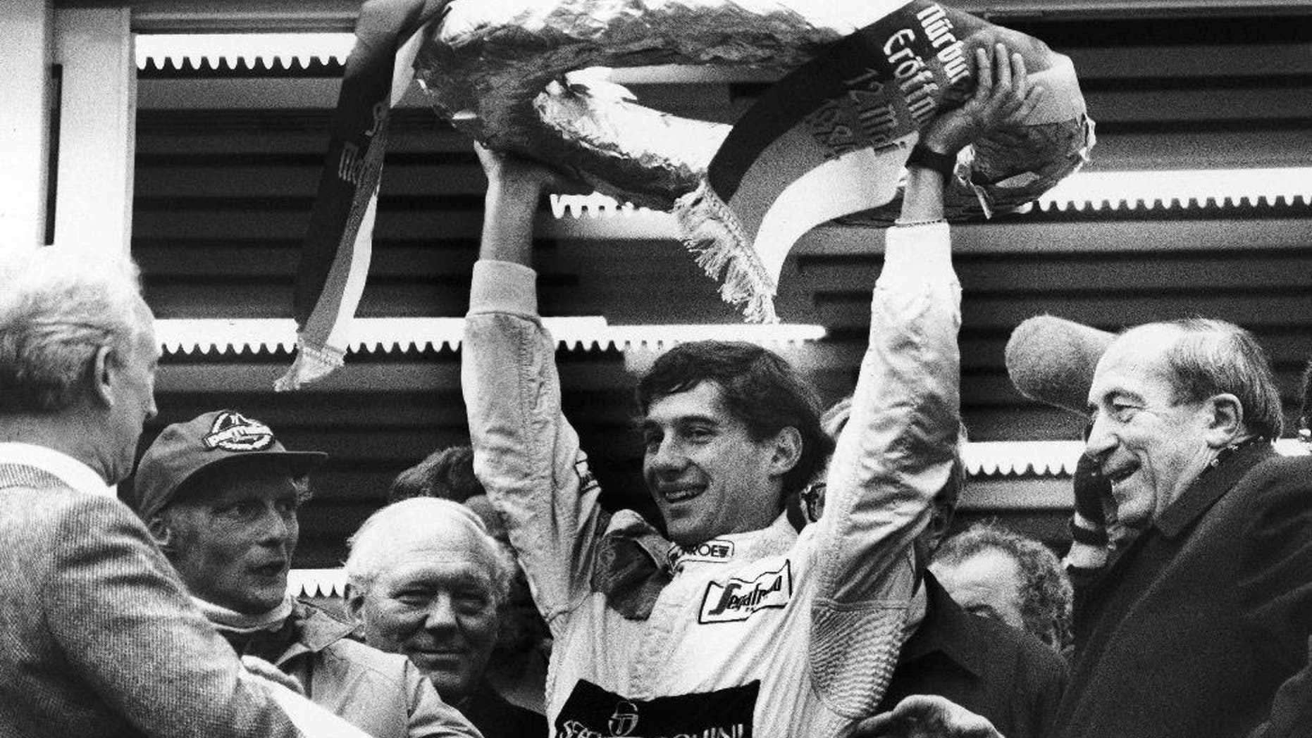 FILE - In this May 13, 1984, file photo, Brazilian Formula One race driver Ayrton Senna da Silva, center, holds up the winner's crown after he won the Mercedes 190 E race in Nuremberg, Germany ahead of former world champion Niki Lauda, second from left. At the right, smiling German transport minister Werner Dollinger. Senna won three Formula One titles — in 1988, 1990 and '91 — all with McLaren. He moved to the Williams team for his tragic 1994 season. Despite his career being cut short when he was 34, his 41 wins stand third all-time behind Michael Schumacher's 91 and rival Alain Prost's 51. He died at the 1994 San Marino Grand Prix. (AP Photo/Udo Weitz, File)