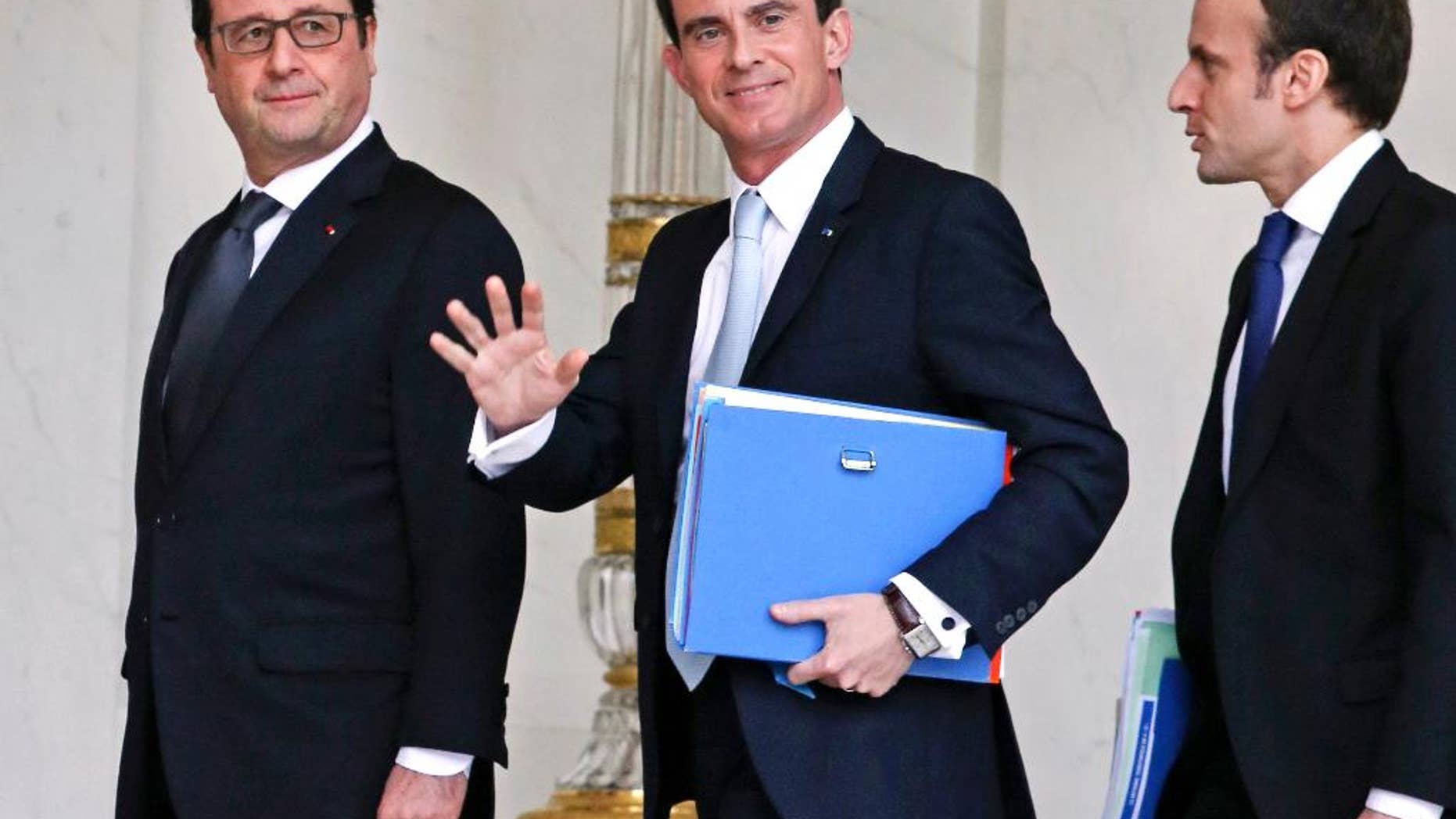 French Prime Minister Manuel Valls, center, waves to reporters as he walks in the lobby of the Elysee Palace with French President Francois Hollande, left, and Economy Minister Emmanuel Macron, right, in February 2015.