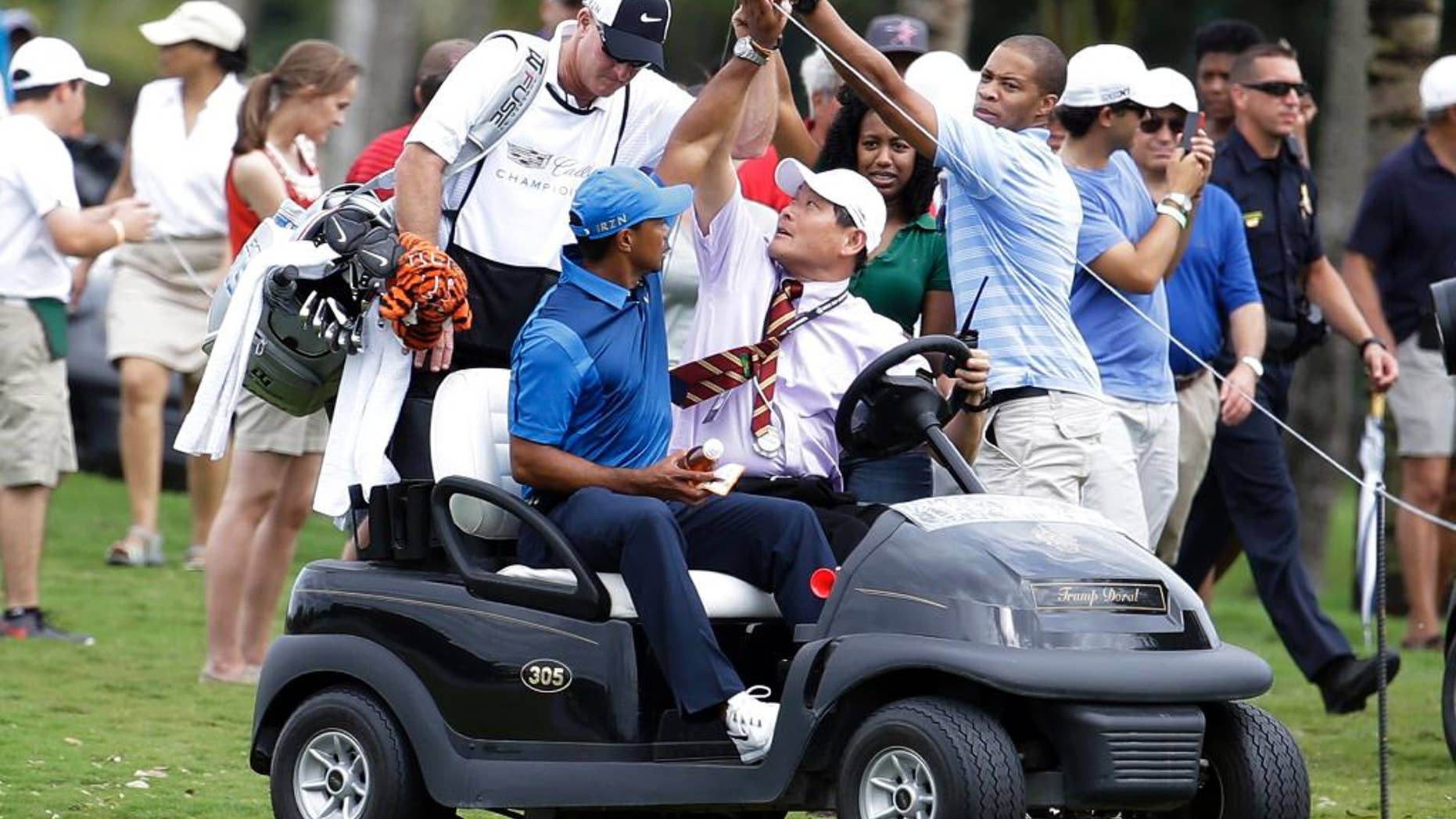 A spectator lifts up a rope as Tiger Woods, left, rides in a cart with his caddy Joe LaCava, center, after play was suspended due to approaching inclement weather during the first round of the Cadillac Championship golf tournament, Thursday, March 6, 2014, in Doral, Fla. (AP Photo/Lynne Sladky)