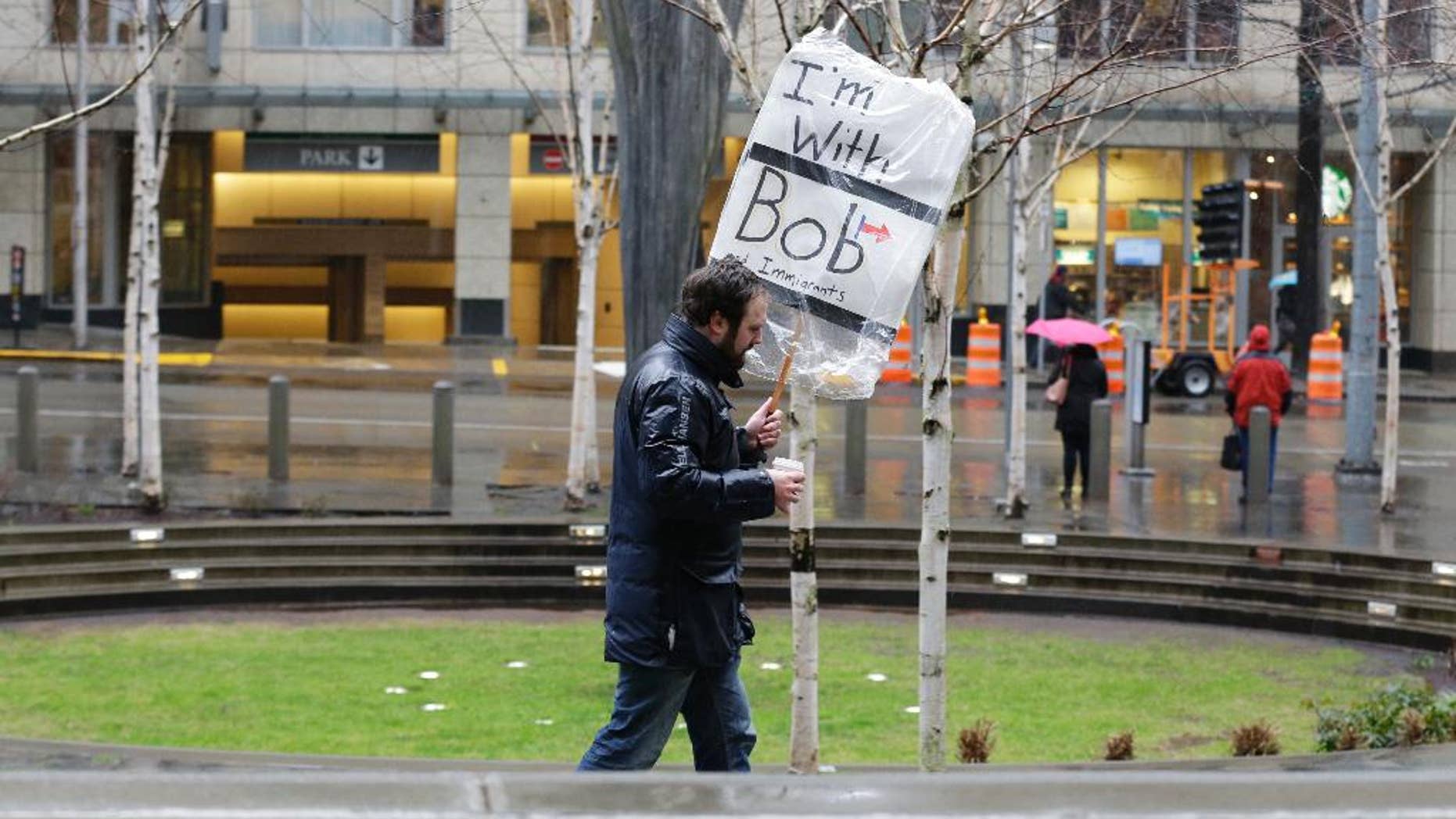 A person walks outside the federal courthouse in Seattle carrying a sign that reads "I'm with Bob and Immigrants," in reference to Washington state Attorney General Bob Ferguson, Friday, Feb. 3, 2017, during a hearing in federal court. A U.S. judge on Friday temporarily blocked President Donald Trump's ban on people from seven predominantly Muslim countries from entering the United States after Washington state and Minnesota urged a nationwide hold on the executive order that has launched legal battles across the country. (AP Photo/Ted S. Warren)
