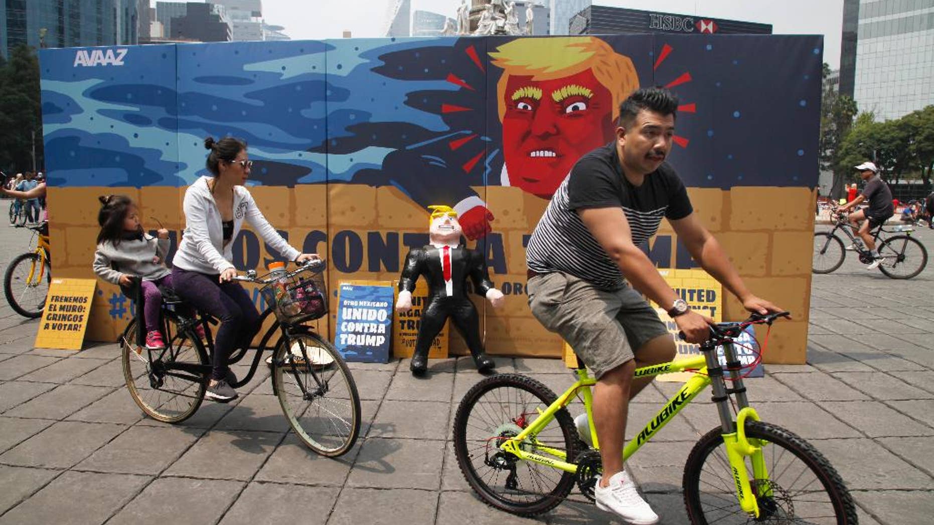 In this Sunday, Sept. 25, 2016 photo, a family of three ride their bicycles past a piñata depicting U.S. Republican presidential nominee Donald Trump propped against a cardboard mural wall with a message in Spanish that reads; "United against Trump" at the Angel of Independence monument in Mexico City. The head of Mexico’s central bank told the Radio Formula network Friday, Sept. 30, 2016, that a Trump presidency “would be a hurricane and a particularly intense one if he fulfills what he has been saying in his campaign.” (AP Photo/Marco Ugarte)