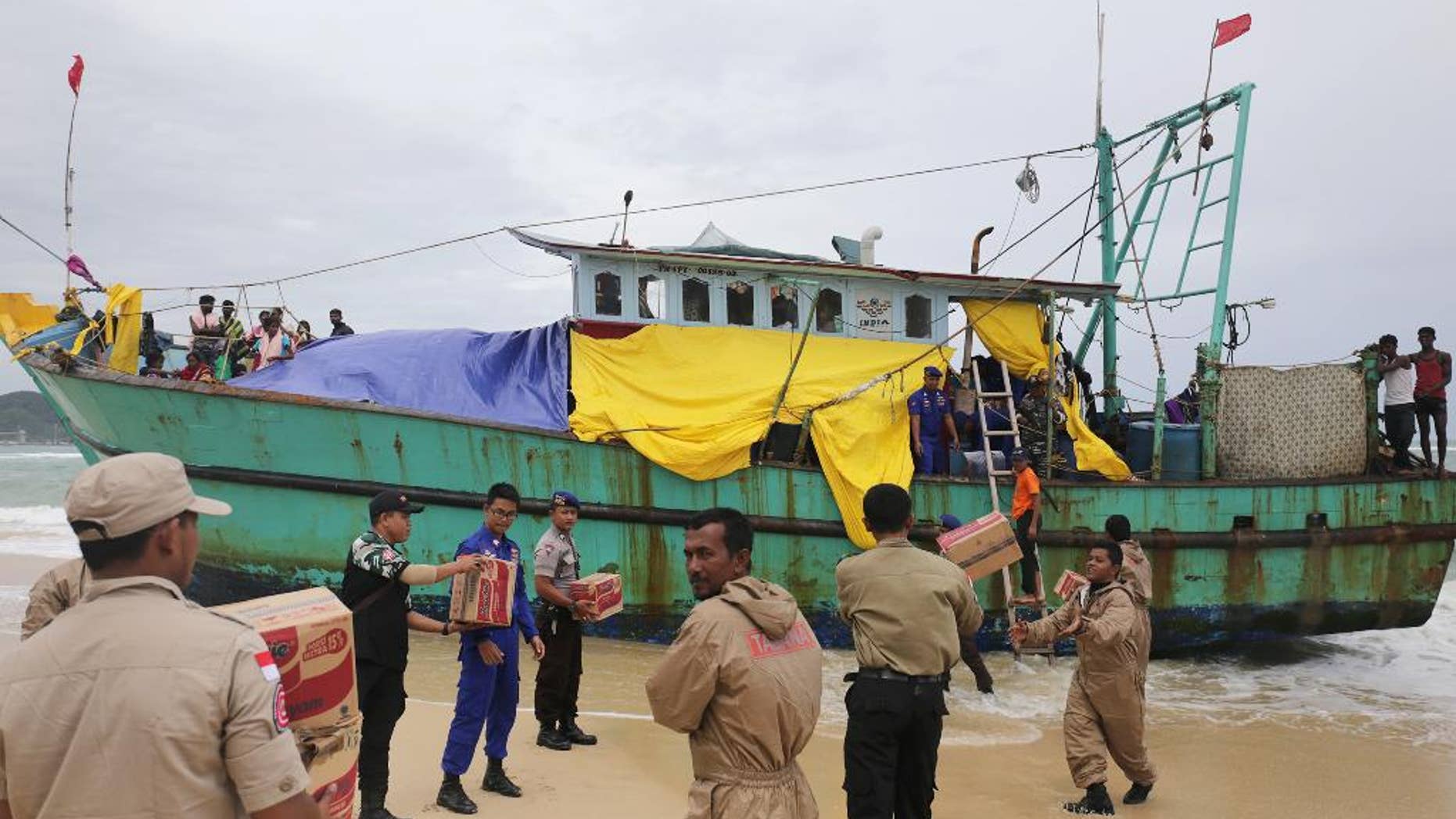 Indonesian officials load food supplies onto a boat carrying Tamil migrants which have been stranded on the beach for the last few days in Lhoknga, Aceh province, Indonesia, Friday, June 17, 2016. Authorities are preparing to tow the boat carryingvdozens of men, women and children out to sea Friday after rescuing it last weekend. (AP Photo/Heri Juanda)