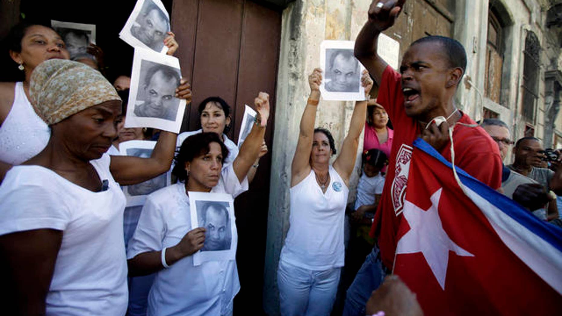 A government supporter, right, chants revolutionary slogans as members of dissident group Ladies in White hold up images of late dissident Orlando Zapata Tamayo on the first anniversary of his death in Havana, Cuba, Wednesday Feb. 23, 2011. Ladies in White is a group of relatives of Cuban dissidents who were or are still imprisoned. (AP Photo/Javier Galeano)
