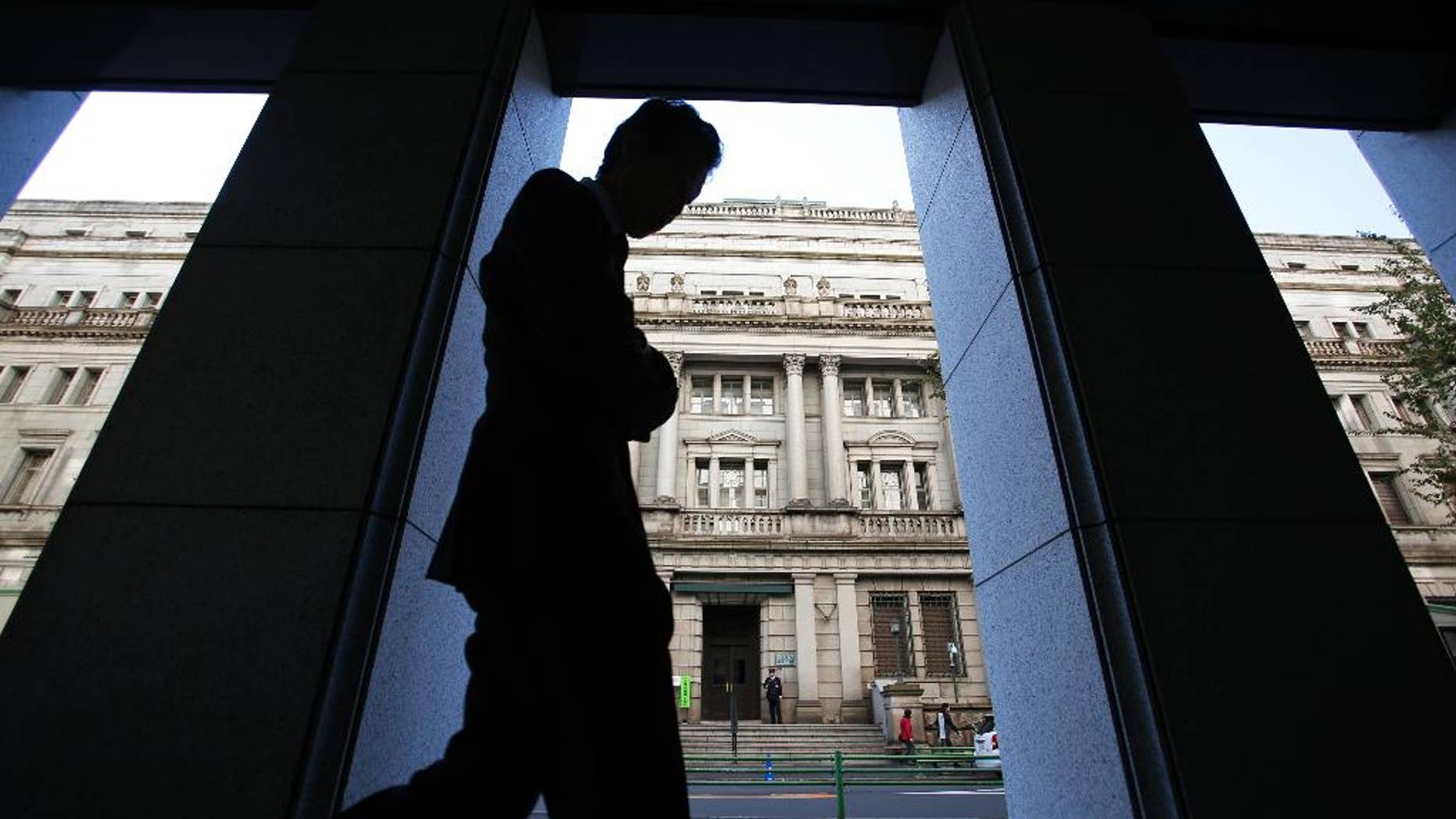 FILE - In this Nov. 19, 2014 file photo, a man walks in front of the Bank of Japan headquarters in Tokyo. Japan's latest data show the economy grew at a real annualized rate of 1.5 percent in October-December, slower than earlier reported but still reaffirming an end to recession. (AP Photo/Shizuo Kambayashi, File)