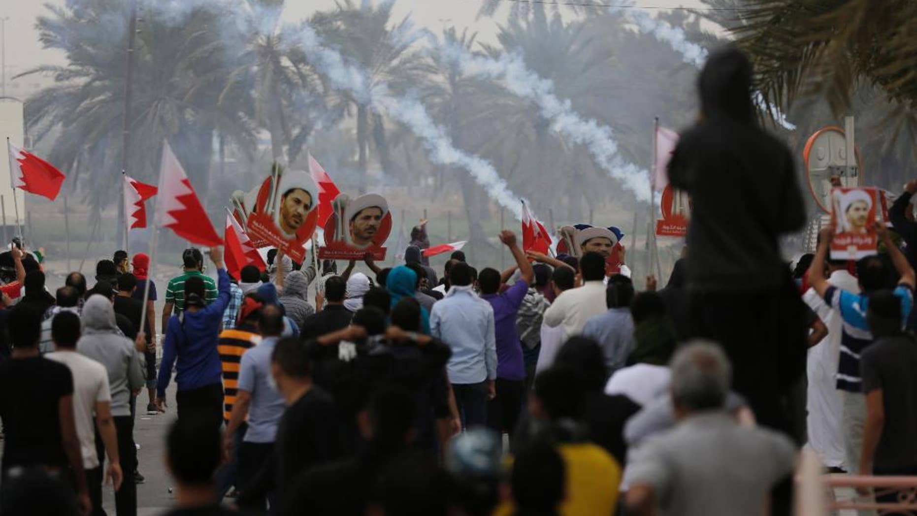 Riot police fire tear gas to disperse Bahraini anti-government protesters waving flags and carrying pictures of jailed Shiite cleric Sheikh Ali Salman, head of the largest opposition political society, Friday, Feb. 13, 2015, in the Manama suburb of Bilad al-Qadeem, Bahrain. Protest marches were held and clashes erupted in opposition areas nationwide Friday, where many shops stayed closed as part of a three-day general strike called by the February 14 opposition youth group before Saturday's fourth anniversary of Bahrain's pro-democracy uprising. (AP Photo/Hasan Jamali)