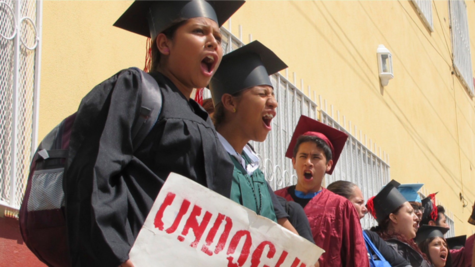 FILE - In this Sept. 20, 2013 file photo, wearing graduation-style caps and gowns, Mexican youth raised in the U.S, chant slogans outside a migrant shelter before crossing the international bridge from Nuevo Laredo, Mexico. A lawyer who traveled to the Texas-Mexico border with the 34 immigrants protesting U.S. immigration policies says 25 of the 26 remaining in federal custody have completed another step in their requests for asylum. (AP Photo/Christopher Sherman, File)