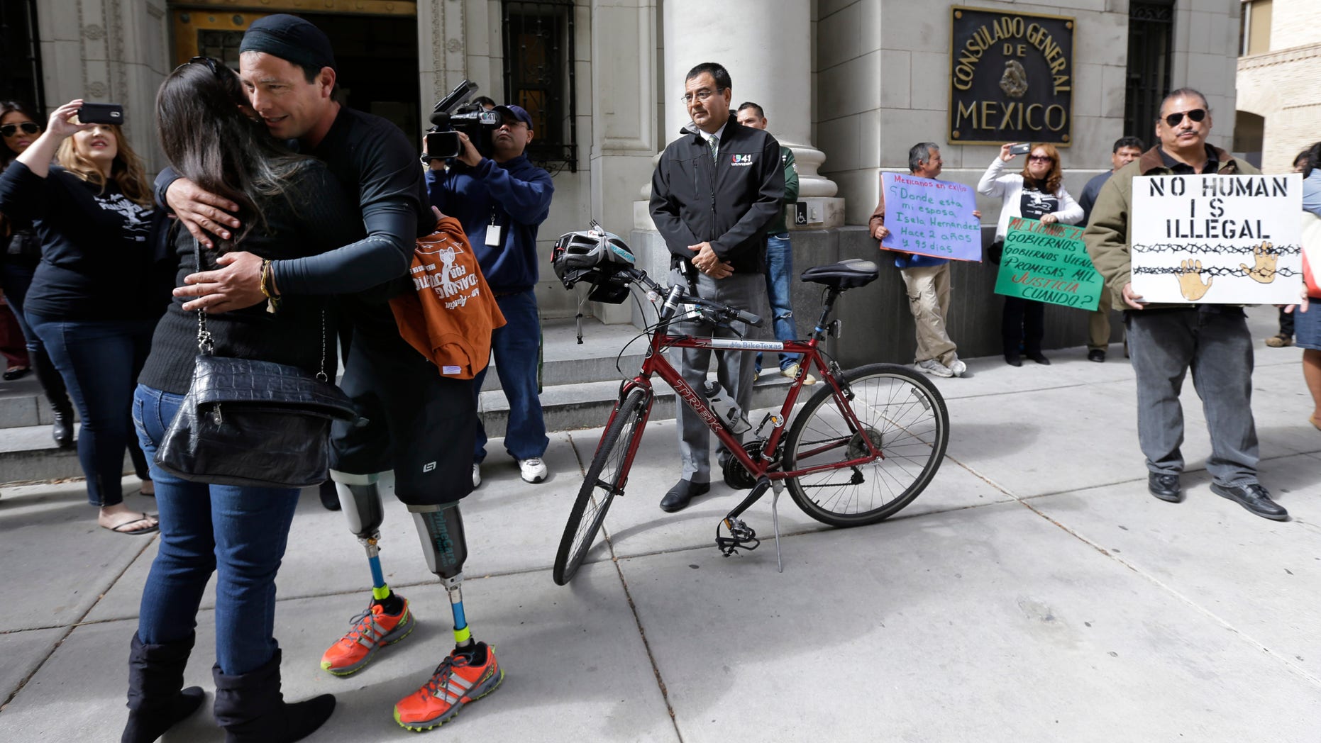 Cyclist Carlos Gutierrez, a double amputee, center, gets a hug from a supporter during a stop at the Mexican Consulate, Thursday, Nov. 7, 2013, in San Antonio. Gutierrez, a Mexican asylum seeker who fled to the U.S. after extortionists cut his legs off for not paying the extortion fees, is riding his bike from El Paso, Texas to Austin, Texas, to raise awareness on the situation of political asylum seekers. (AP Photo/Eric Gay)