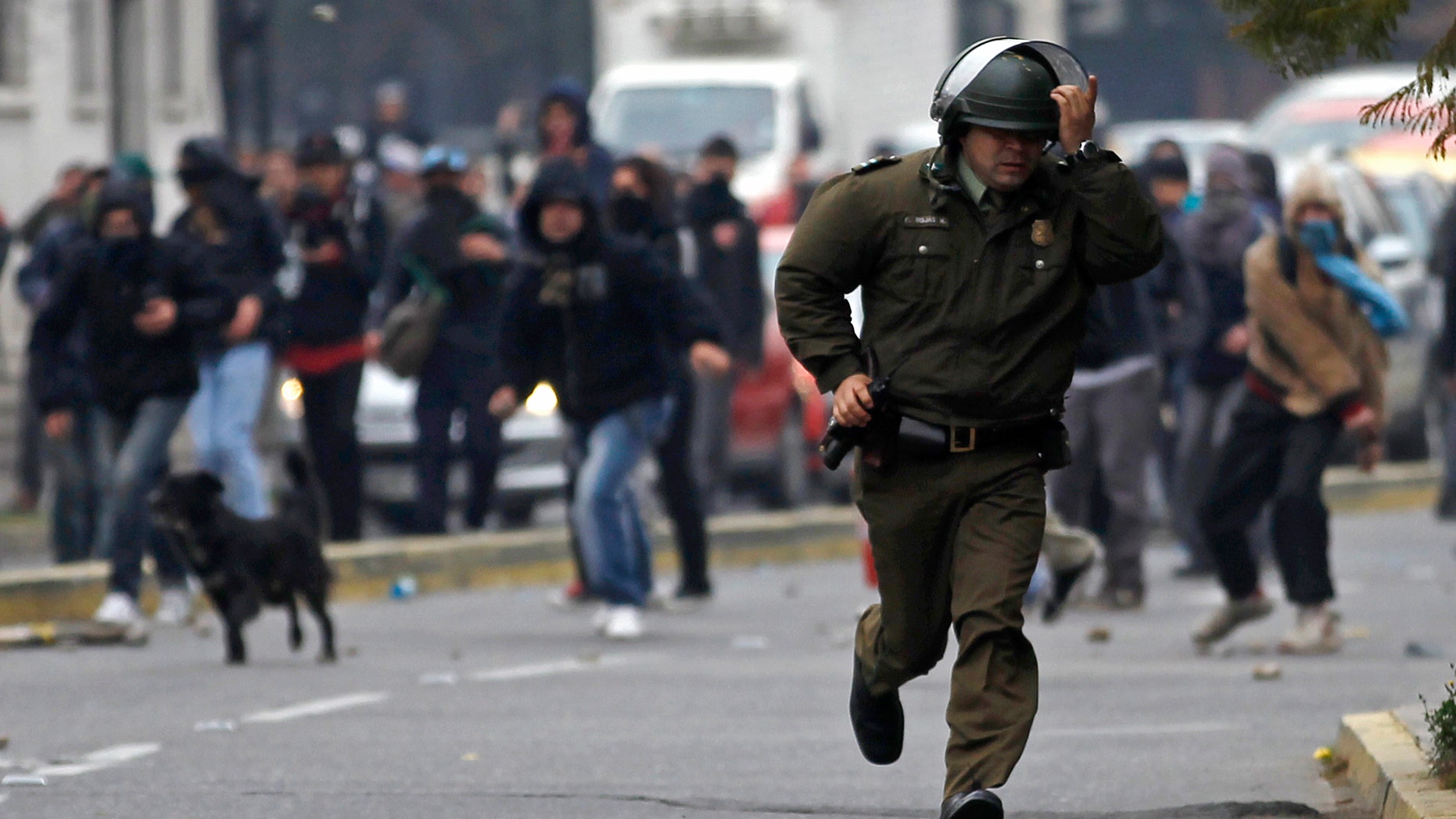 A police officer runs from hooded protestors throwing stones during student demonstrations in Santiago, Chile, Thursday Aug. 4, 2011.