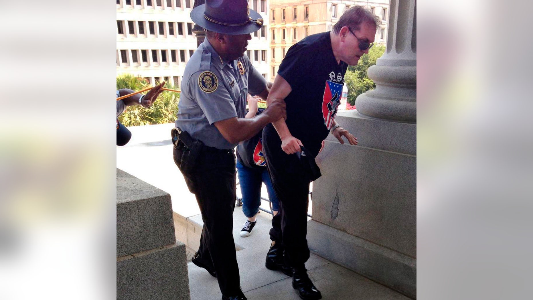 In this photo provided by Rob Godfrey, police officer Leroy Smith, left, helps a man wearing National Socialist Movement attire up the stairs during a rally Saturday, July 18, 2015, in Columbia, S.C. Members of the group were protesting Saturday the removal of the Confederate flag from the Statehouse grounds earlier this month. (Rob Godfrey via AP)