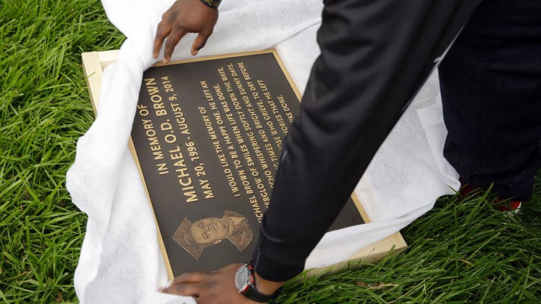 Michael Brown Sr. unwraps a plaque remembering his son, Michael Brown, to show volunteers as they remove items left at a makeshift memorial to Michael Brown Wednesday, May 20, 2015, in Ferguson, Mo. The memorial that has marked the place where Brown was fatally shot by a police officer in August has been removed and will be replaced with a permanent plaque. (AP Photo/Jeff Roberson)