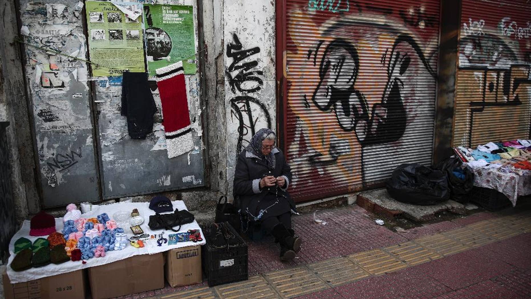 A woman knits as she sits next to her stall in Piraeus port town, west of Athens, on Tuesday, March 10, 2015. Greece is quickly running out of cash and has to repay debts this month to the International Monetary Fund — which co-funded Greece's euro240 billion bailout . (AP Photo/Yorgos Karahalis)