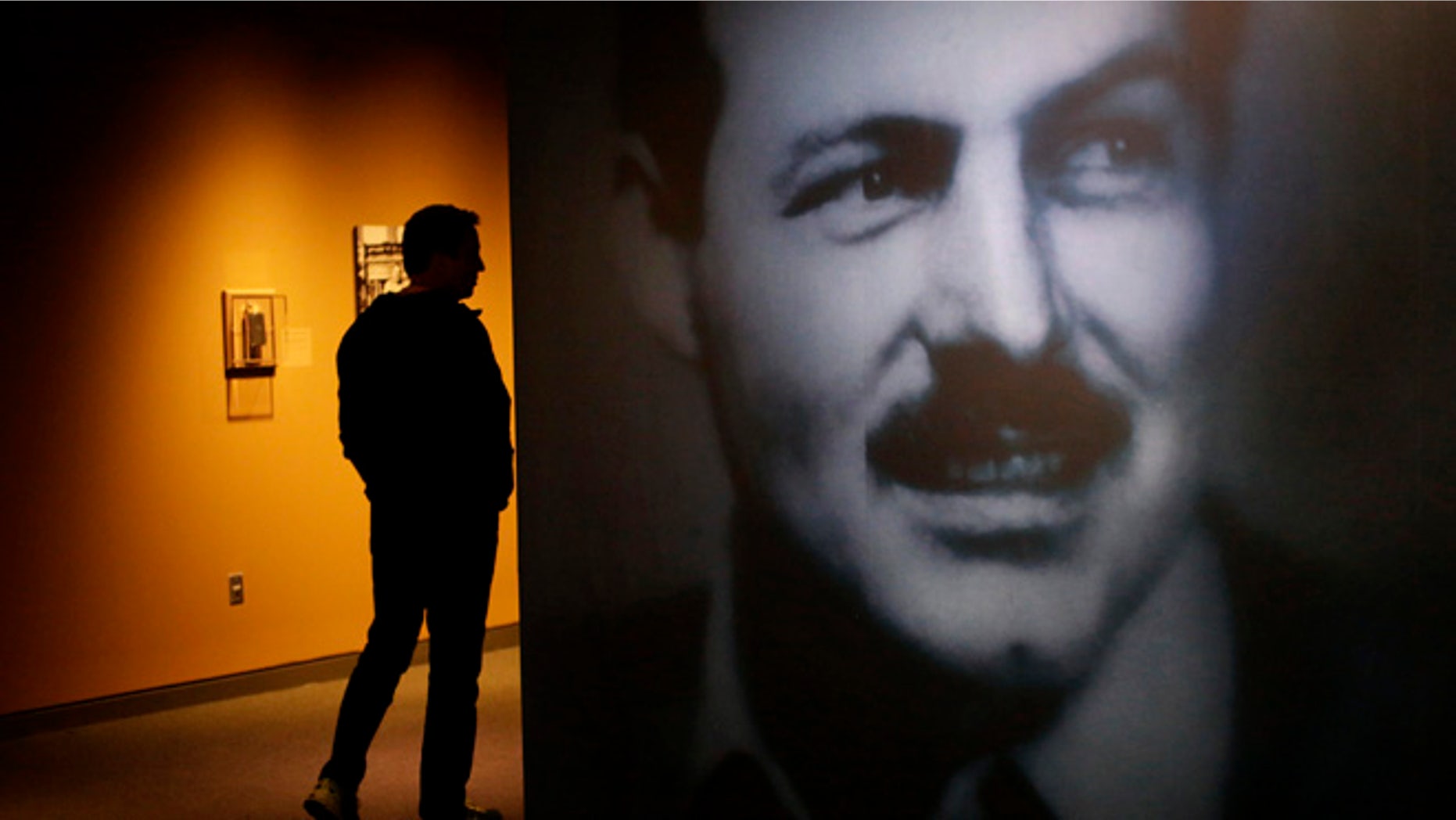 A museum visitor, left, walks past a photograph of Ernest Hemingway in the exhibit: "Ernest Hemingway: Between Two Wars" at the John F. Kennedy Presidential Library and Museum on Tuesday, April 12, 2016, in Boston. Original drafts of Ernest Hemingway works along with personal items are on display for the first time at the museum. (AP Photo/Steven Senne)