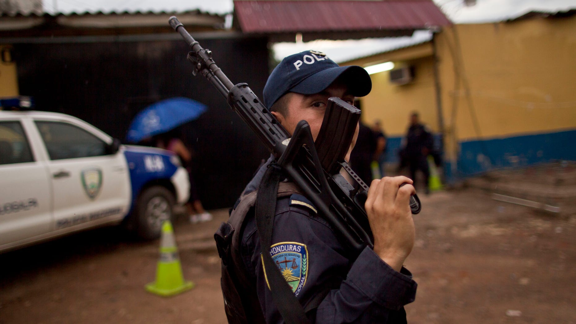 In this June 1, 2013 photo, a National Police officer looks from behind his weapon during an operative outside a police station near El Mayoreo markert in Tegucigalpa, Honduras. The government of Honduras launched an unprecedented effort last year to clean up a U.S.-backed police force widely seen as deeply brutal and corrupt. One by one, hundreds of police officers were subjected to polygraph tests administered by Colombian technicians funded by the U.S. government. Nearly four of every 10 officers failed the test in the first five months it was administered, some giving answers that indicated that they had, among other violations, tortured suspects, accepted bribes and taken drugs, according to a confidential U.S. document provided to The Associated Press. (AP Photo/Esteban Felix)