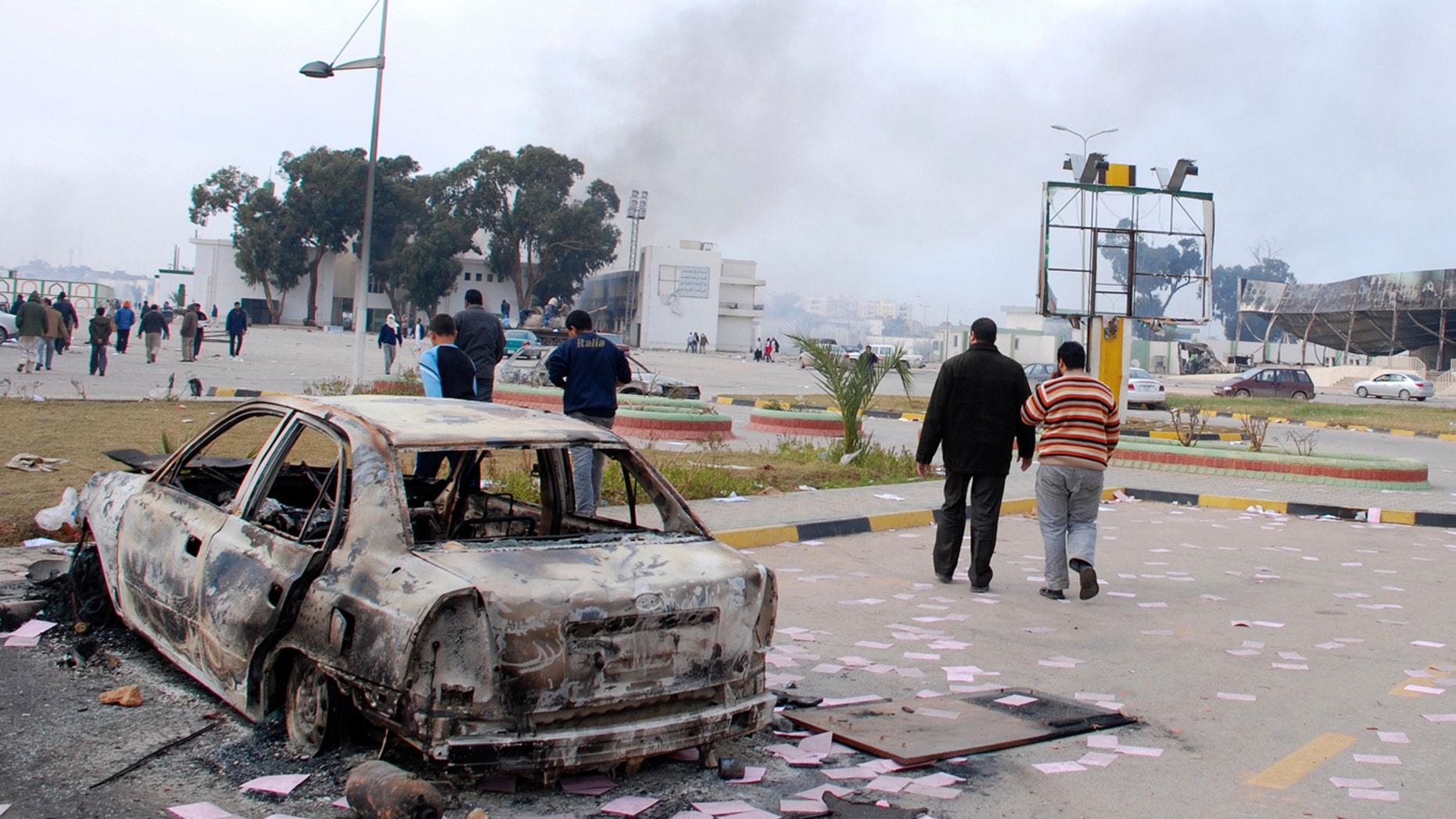 Feb. 21: Residents are seen walking past a burned-out vehicle in Benghazi, Libya. Stocks have dropped and oil prices are on the rise as protests sweep through the Libya.