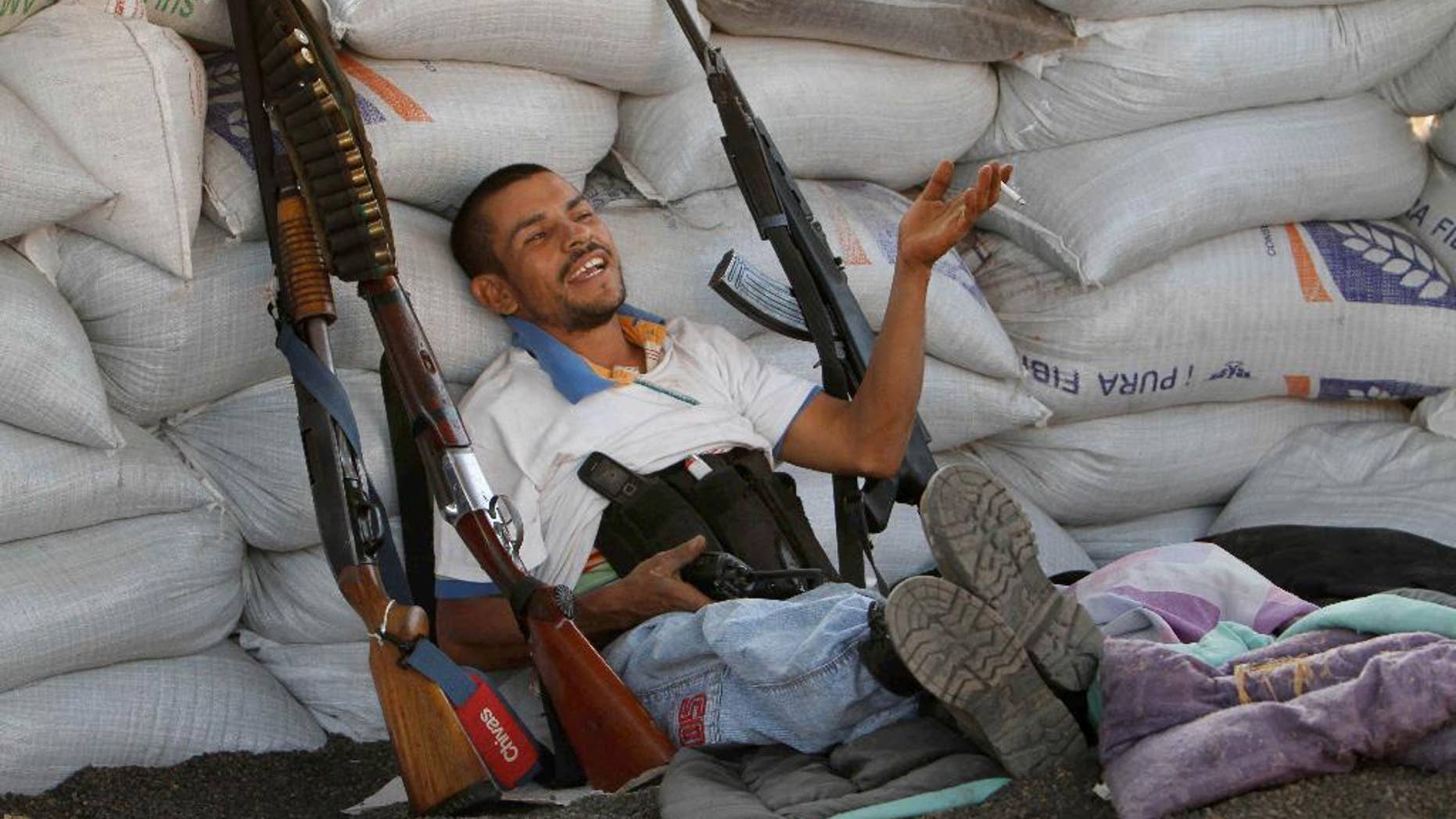 FILE- In this Feb. 9, 2014, file photo, flanked by weapons a man from a self-defense group sits inside a barricade at the entrance of Apatzingan in Michoacan state, Mexico. Vigilantes who have driven a quasi-religious drug cartel from a series of towns in western Mexico entered Apatzingan on Saturday and were working with government forces to clear it of cartel gunmen. The Mexican government announced Tuesday April 15, 2014, that vigilante groups in the western state of Michoacan will have until May 10 to register their guns and decide whether to join the army’s “rural defense corps.” (AP Photo/Marco Ugarte File)