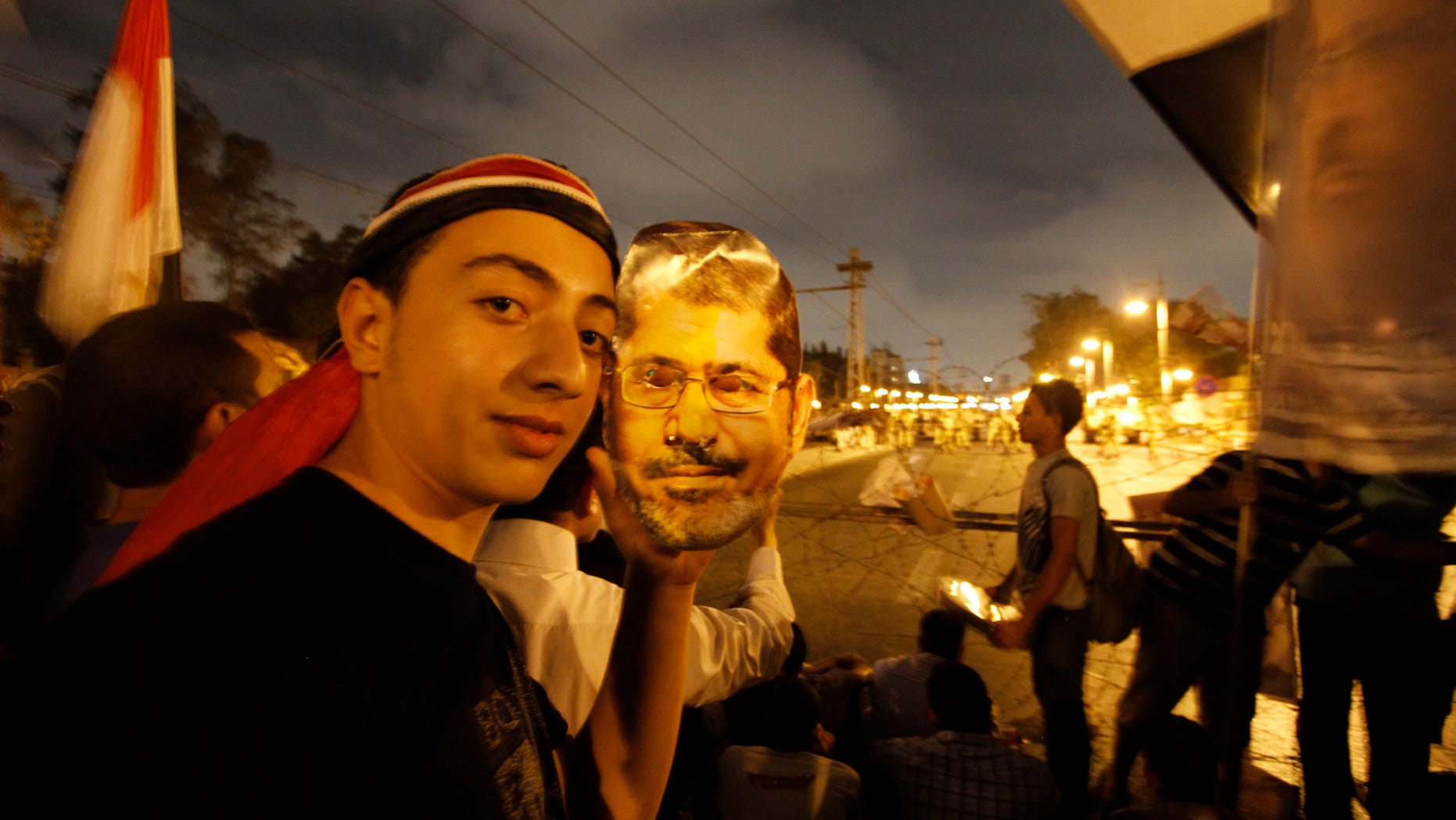 A supporter of Egypt's ousted President Mohammed Morsi poses with a paper mask of Morsi as he and others face the Egyptian military soldiers near the presidential palace in Cairo, Egypt, Saturday, July 13, 2013. Tens of thousands of Islamists rallied Friday in cities across Egypt, vowing to sustain for months their campaign to restore deposed President Mohammed Morsi to power. (AP Photo/Nasser Shiyoukhi)