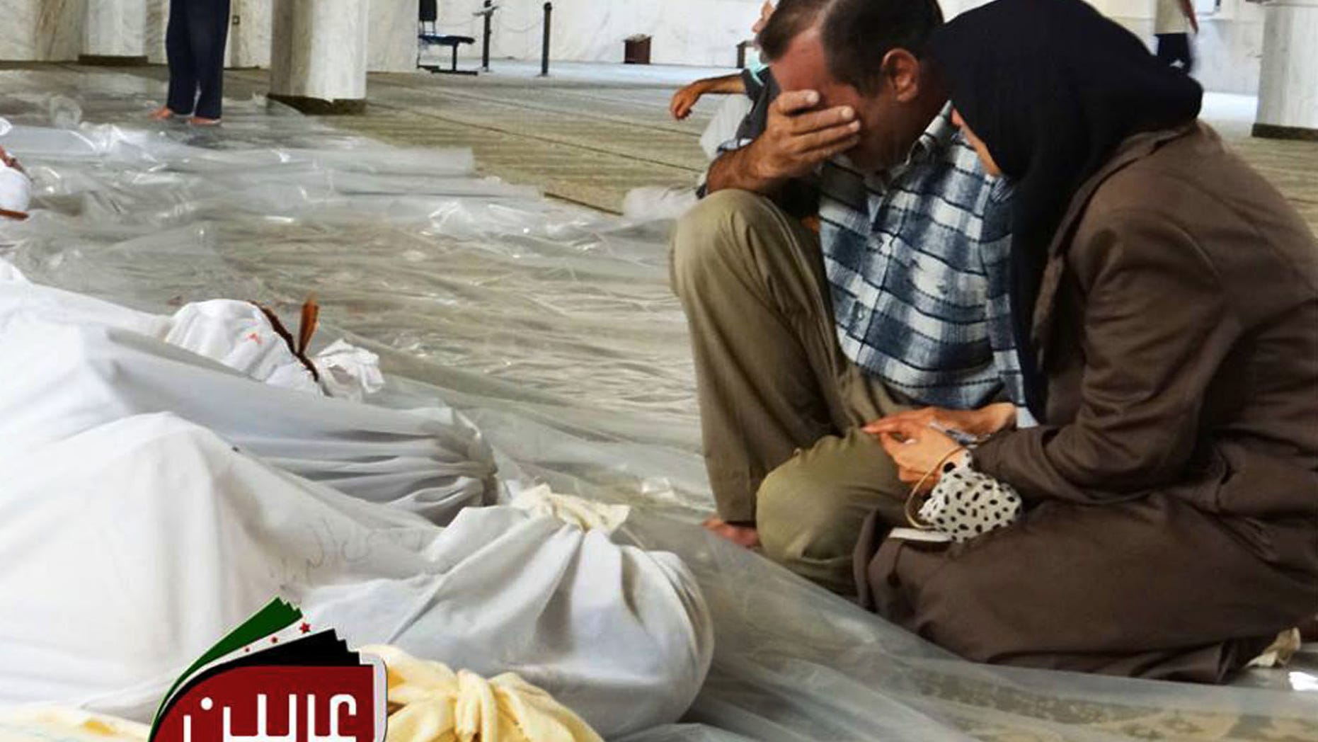 In this citizen journalism photo provided by the Local Committee of Arbeen, which has been authenticated based on its contents and other AP reporting, a man and woman mourn over the dead bodies of Syrian men after an alleged poisonous gas attack fired by regime forces, according to activists in Arbeen town, Damascus, Syria, Wednesday, Aug. 21, 2013. Syrian regime forces fired intense artillery and rocket barrages Wednesday on the eastern suburbs of the capital Damascus, in what two pro-opposition groups claimed was a "poisonous gas" attack that killed dozens of people. (AP Photo/Local Committee of Arbeen)