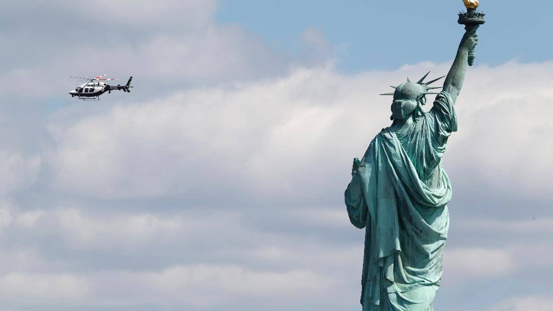 A New York Police helicopter circles over Liberty Island where the Statue of Liberty was evacuated with officers responding to a report of a suspicious package seen from Jersey City, N.J., Friday, April 24, 2015. Visitors are posting photos online showing hundreds of people being herded toward a ferry landing. Tourists say they were taken off boats while trying to leave nearby Ellis Island. Those vessels then were used to evacuate Liberty Island. (AP Photo/Julio Cortez)