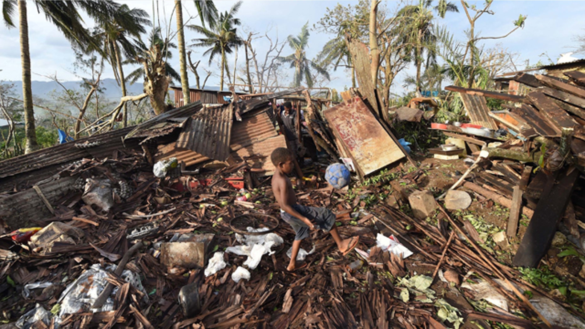 March 16, 2015: Samuel, only his first name given, kicks a ball through the ruins of their family home as his father, Phillip, at back, picks through the debris in Port Vila, Vanuatu in the aftermath of Cyclone Pam. (AP)