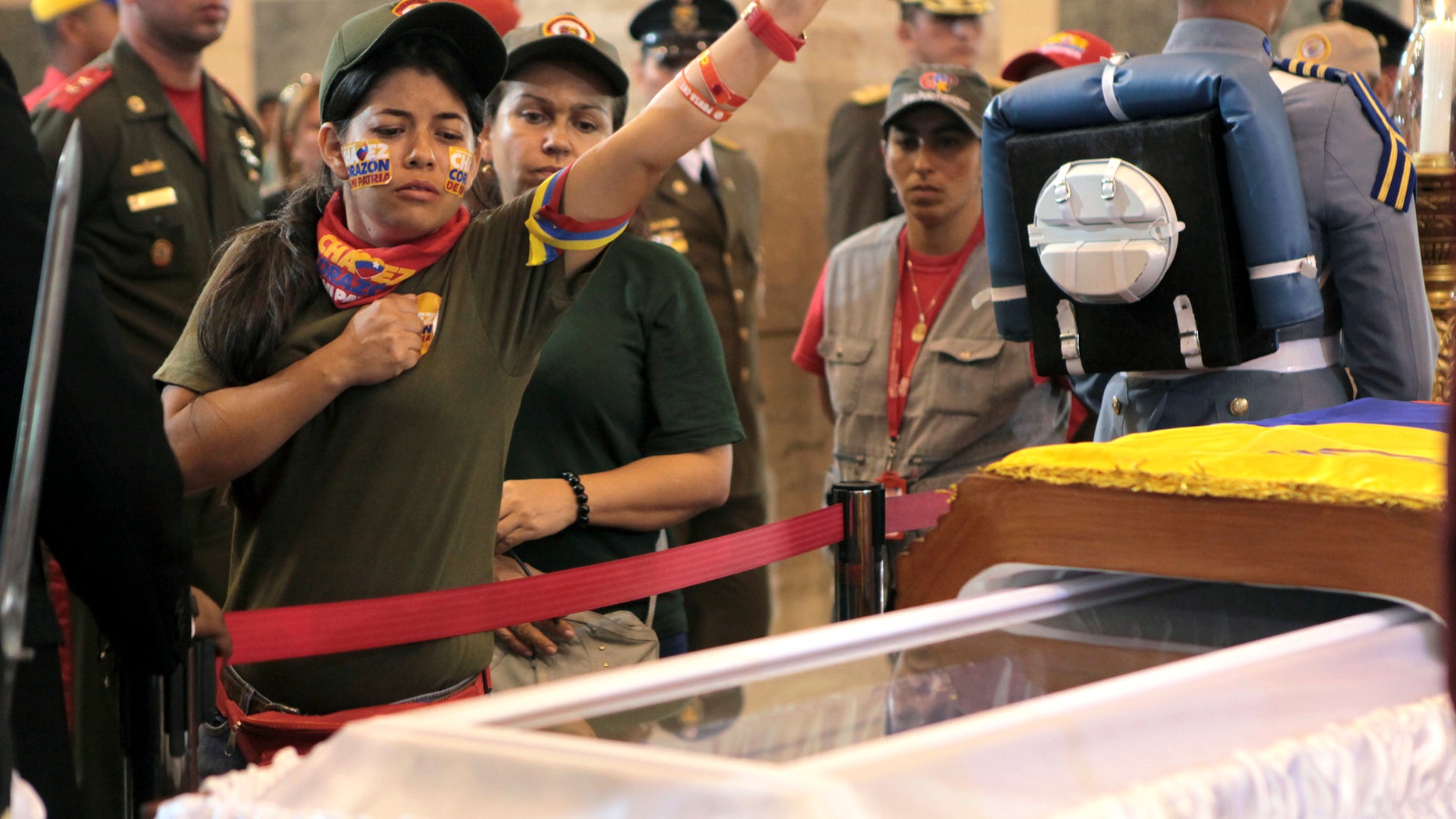 March 7, 2013: In this photo released by Miraflores Press Office, a woman pays her respects, placing a hand on her heart and saluting, before she files past the glass-topped casket containing the remains of Venezuela's late President Hugo Chavez at the military academy, where he started his army career, in Caracas.