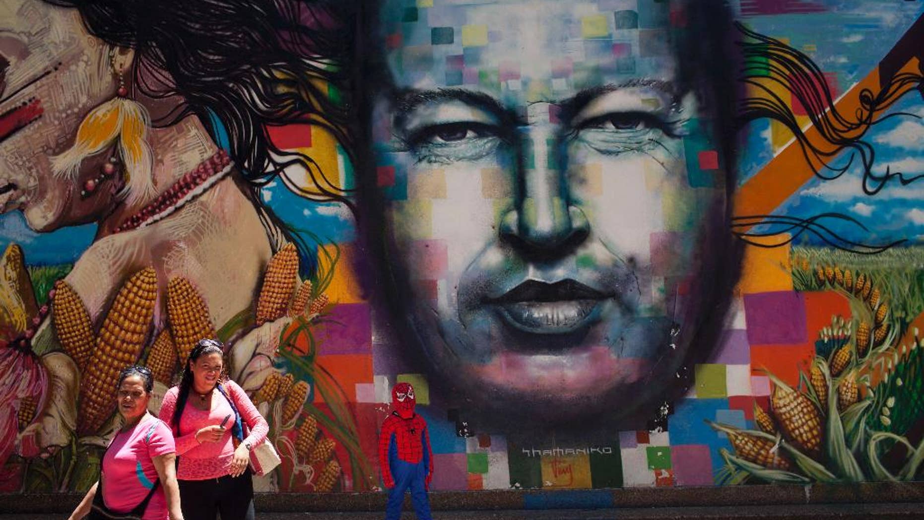 A boy dressed in a Spiderman costume poses for a photo next to a mural of Venezuela's late President Hugo Chavez painted on a wall of the Museo de Bellas Artes in Caracas, Venezuela, Tuesday, March 4, 2014. He’s been dead a year, but Chavez’s face and voice are everywhere. He bangs out the national anthem on state radio every morning and the national guard has even blasted his voice reciting poetry to drive rock-throwing protesters off the street. (AP Photo/Rodrigo Abd)