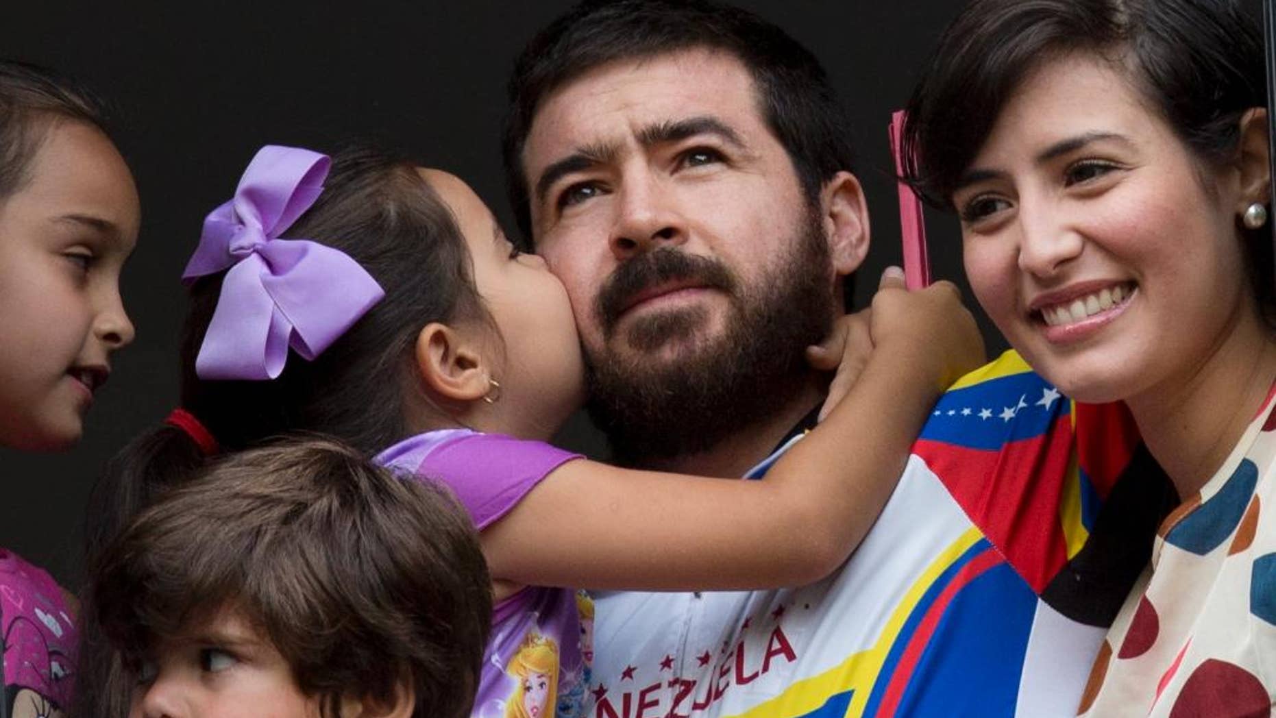 Maria Daniela kisses her father Daniel Ceballos, former mayor of the western city of San Cristobal, as he looks out from an apartment window with his wife Patricia de Ceballos, right, daughter Maria Veronica, left, and son Juan Daniel in Caracas, Venezuela, Wednesday, Aug. 12, 2015. One of Venezuela's most prominent opposition leaders started his first day of house arrest Wednesday after a surprise release following a year and a half in prison. The 31-year-old leader, who is awaiting trial on charges of civil rebellion, suffered from kidney and stomach problems during a 20-day hunger strike in June, according to his supporters. (AP Photo/Ariana Cubillos)