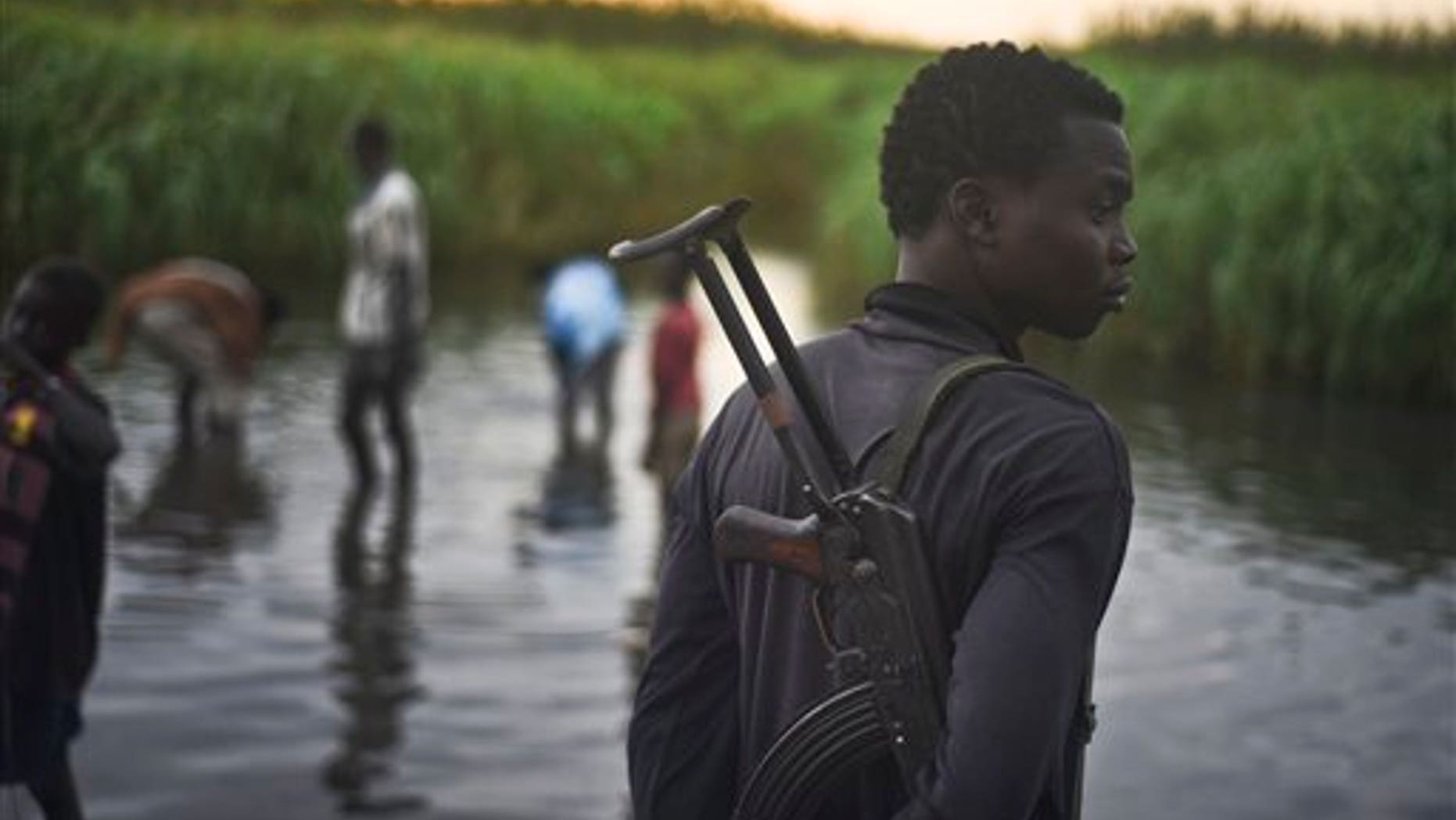 An unidentified man with a gun stands watch over displaced people who have taken shelter from fighting, in a rebel-held part of Leer county in South Sudan Oct. 12. (AP Photo/Jason Patinkin)