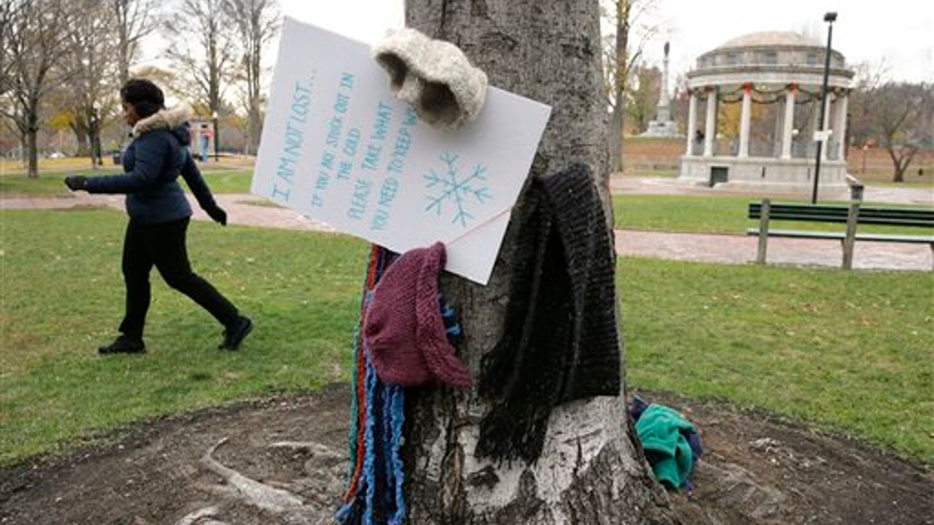 Hats and scarves hang on a tree near a sign that invites people in need to take them to keep warm, on the Boston Common Tuesday, Dec. 8, 2015, in Boston. A Good Samaritan has been hanging the cold weather items, as well as coats, gloves, and mittens, for the needy on trees in the park, a gesture that's warming the hearts of passersby. (AP Photo/Steven Senne)