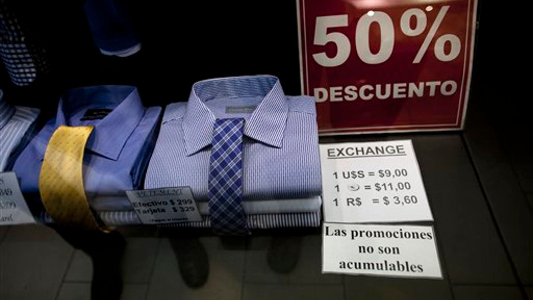 In this June 5, 2013 photo, a shop window displays a sign that reads in Spanish "50% discount" as well as the store's accepted rates of exchange in the informal market for the Argentine peso with the US dollar, the euro, and Brazil's real, along Florida street in Buenos Aires, Argentina. The weakening peso has led to a flood of day-trippers from neighboring countries into Argentina, which imposed severe currency controls in hopes of reducing the flight of dollars and protecting foreign reserves. (AP Photo/Natacha Pisarenko)