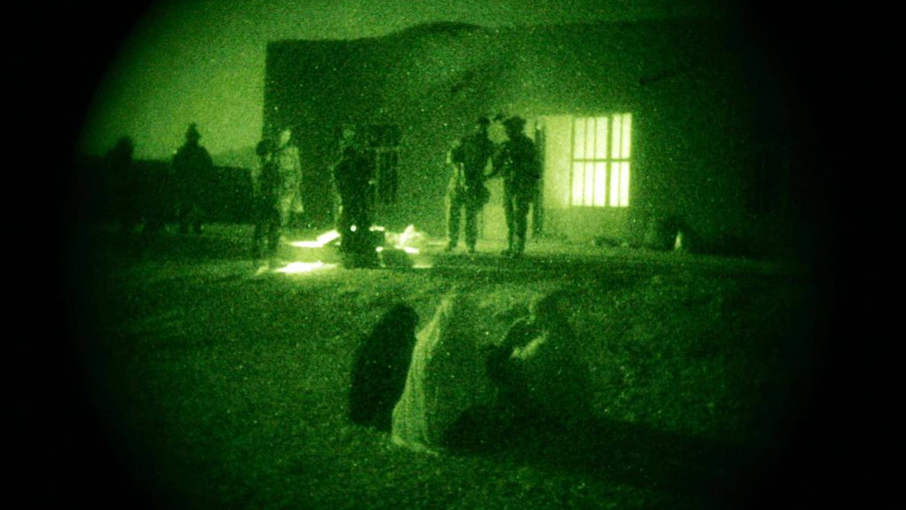 FILE - In this Oct. 28, 2009 file photo taken with a night vision scope, Afghan women and their children wait as U.S. Special Operations forces and Afghan National Army soldiers search their home during a joint operation targeting insurgents operating in Afghanistan's Farah province. Afghan President Ashraf Ghani has ordered a top-to-bottom review of the practices of the country’s defense forces, including discussing a possible resumption of controversial night raids banned by his predecessor, The Associated Press has learned. The move appears aimed at revamping the military for the fight against the Taliban amid new indications that U.S. and international forces will play a greater role than initially envisaged. (AP Photo/Maya Alleruzzo, File)