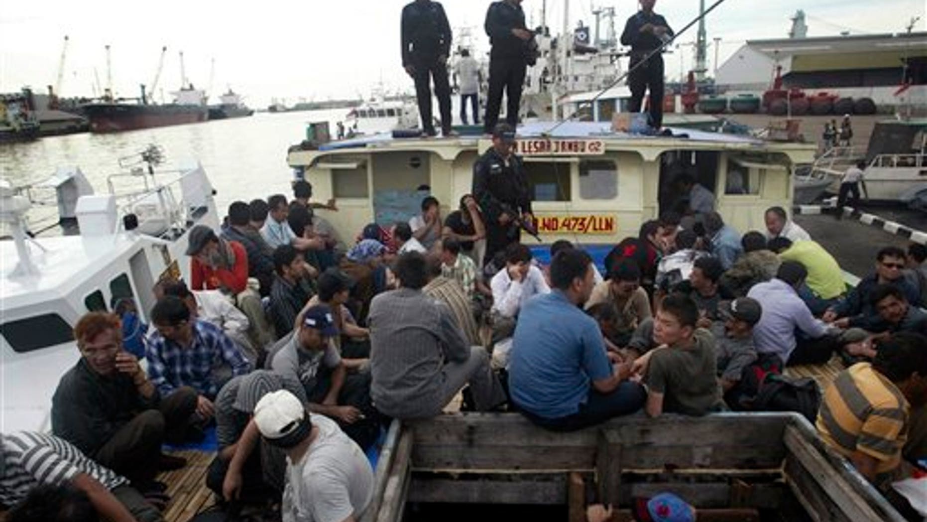 May 2, 2010: Indonesian marine police officers watch as Afghan asylum seekers sit on their ship that was caught off Java island upon docking at Tanjung Perak port in Surabaya, East Java, Indonesia.