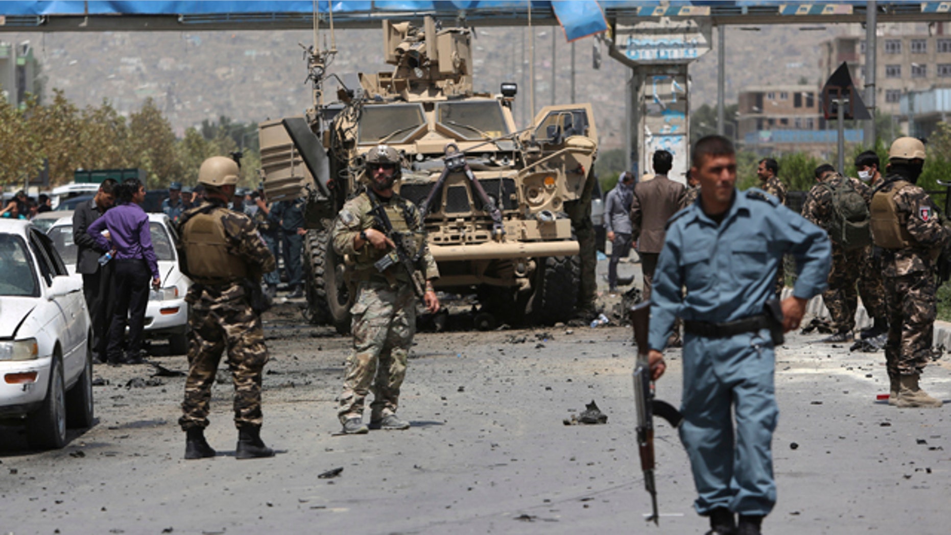 August 10, 2014: NATO and Afghan security forces stand guard at the site of a suicide attack in Kabul. A suicide car bomber attacked a NATO convoy, killing several civilians and wounding more than 35 in an assault claimed by the Taliban, authorities said. (AP Photo/Rahmat Gul)