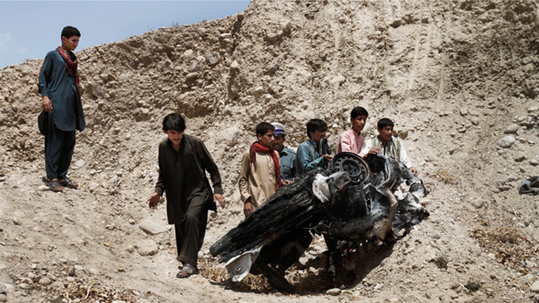 Aug. 12, 2012: Afghans push parts of a damaged vehicle off a hill after a roadside explosion on the outskirts of Laghman province east of Kabul, Afghanistan.