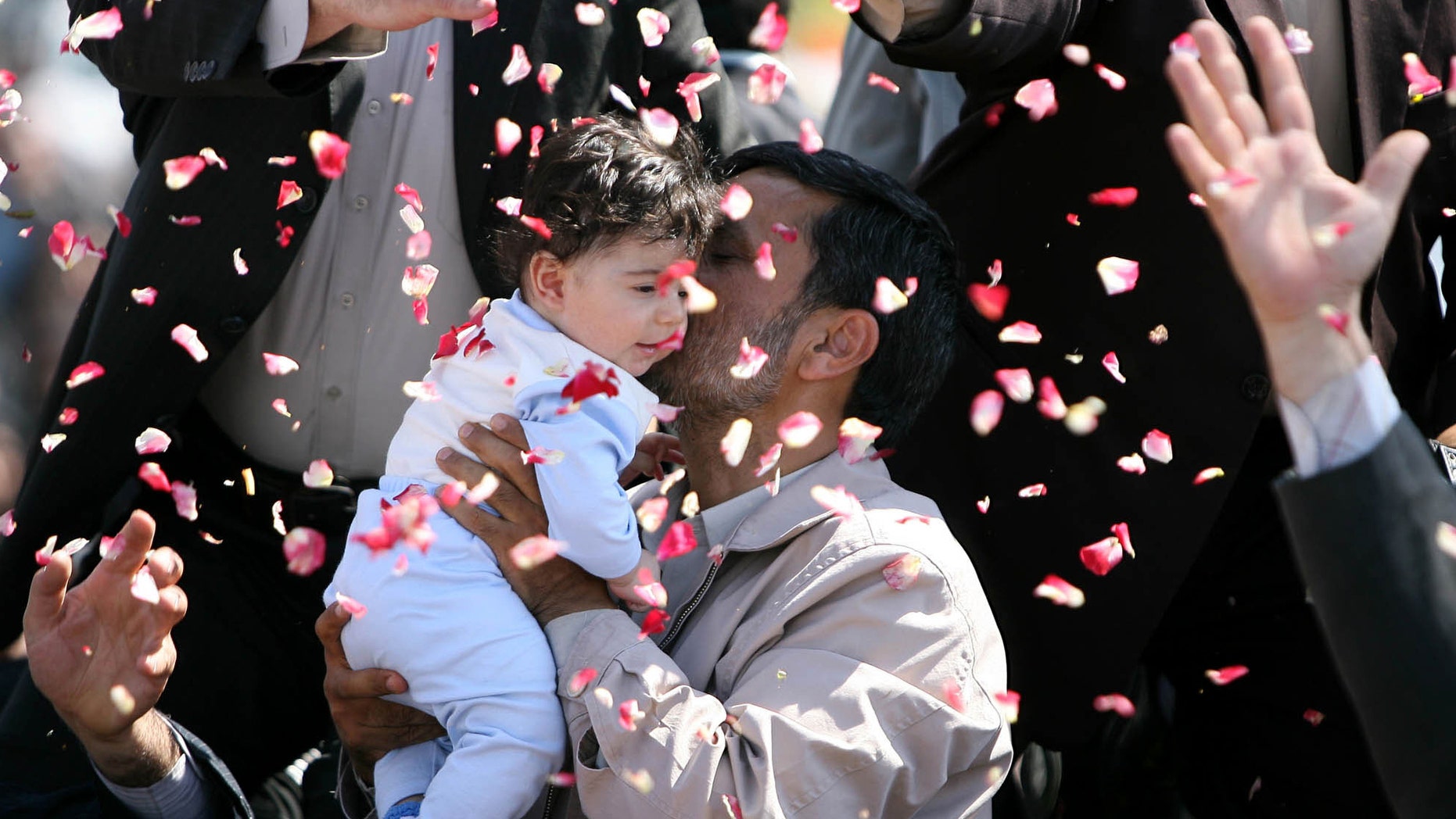 In this May, 20, 2009 photo, Iran's President Mahmoud Ahmadinejad hugs a child and is showered with flower petals during his visit to Semnan, Iran. Iranian President Mahmoud Ahmadinejad inaugurated a new policy on July 27, 2010 to encourage population growth, whereby the government will pay families for every new child. (AP)