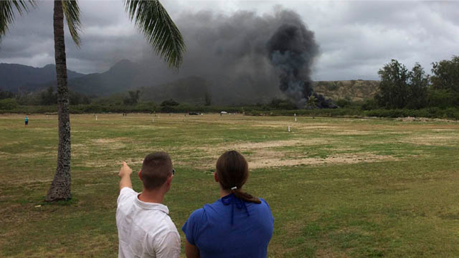 May 17, 2015: A man and woman look toward smoke rising from a Marine Corps Osprey aircraft after making a hard landing on Bellows Air Force Station near Waimanalo, Hawaii. The fatal crash of the Marine Corps' new hybridized airplane-and-helicopter aircraft during a training exercise is renewing safety concerns about the machine. (Zane Dulin via AP)