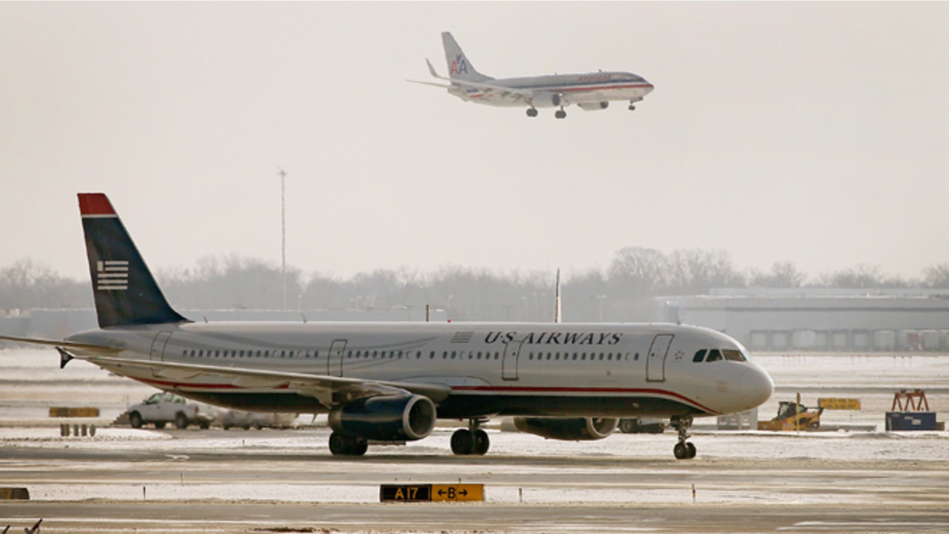 CHICAGO, IL - DECEMBER 09: An American Airlines jet flies over a US Airways jet at O'Hare Airport on December 9, 2013 in Chicago, Illinois. American Airlines announced today that it had completed a merger deal with US Airways. The deal will make American Airlines the world's largest airline, flying about 6,700 flights per day. (Photo by Scott Olson/Getty Images)