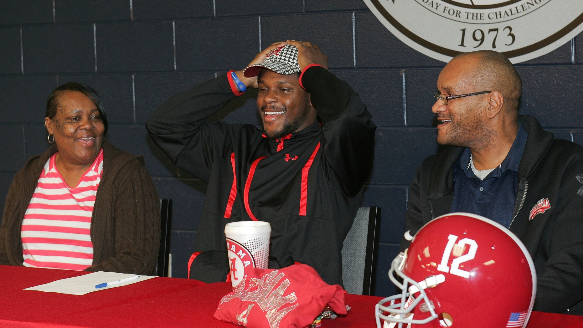 Bob Jones High School football player Reggie Ragland puts on an Alabama hat as mom Ann White and dad Reggie Ragland Sr., look on, after announcing his intentions to attend the University of Alabama and play football during national signing day, Wednesday, Feb. 1, 2012, at Bob Jones High School in Madison, Ala. (AP Photo/The Huntsville Times, Robin Conn)