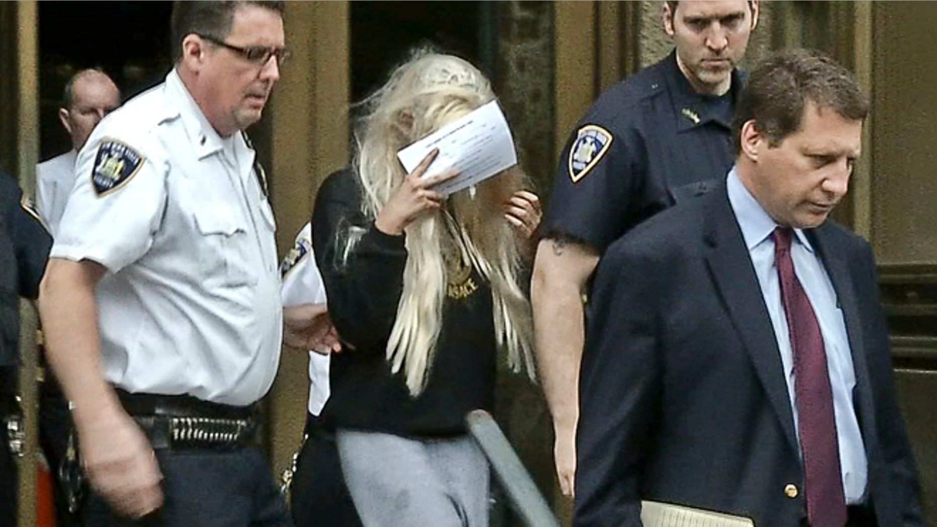 May 24, 2013: In an image made from video, actress Amanda Bynes, center, wearing sweats and a blonde wig, shields her face as she is escorted after a Manhattan criminal court appearance in New York.