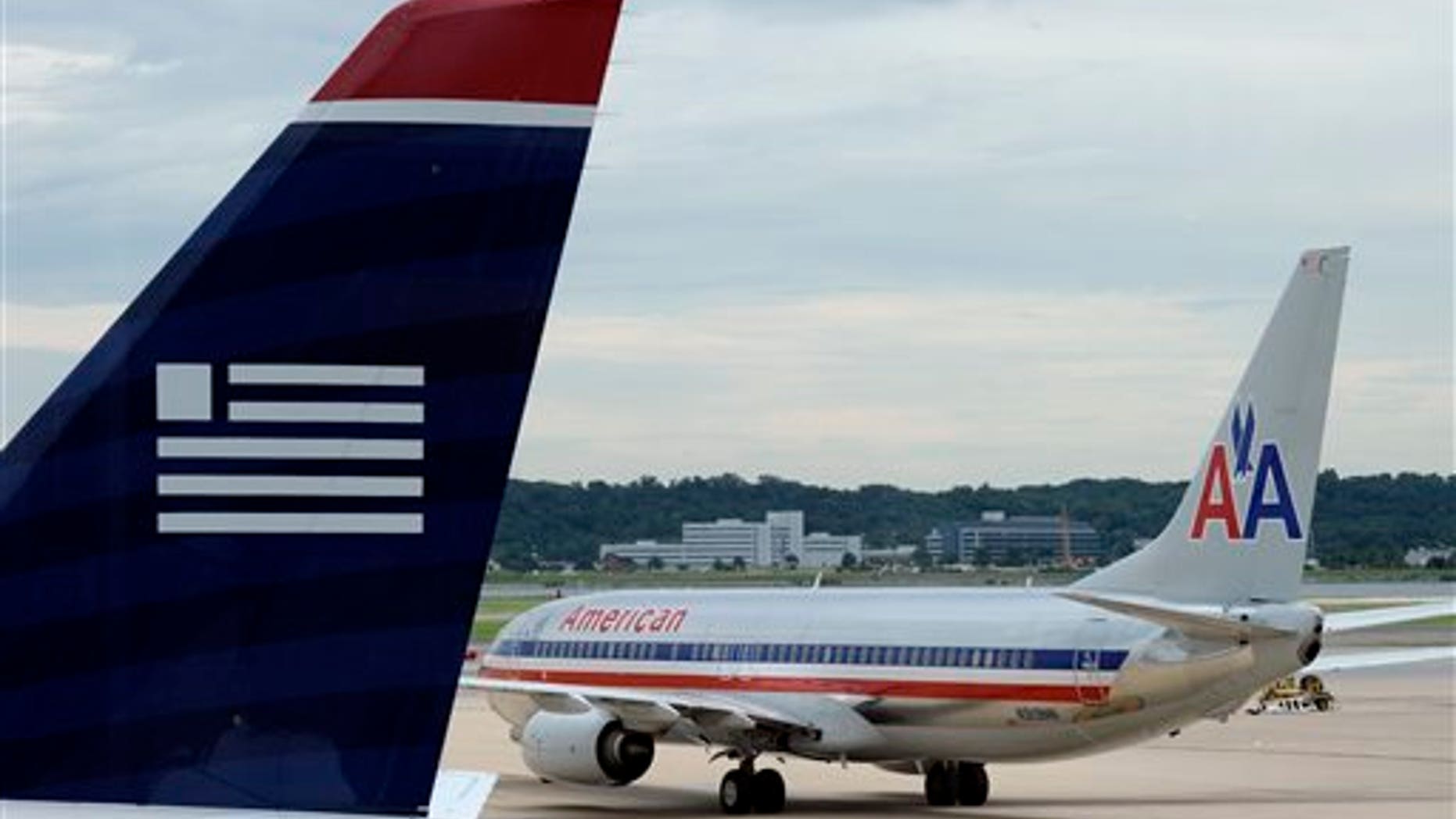FILE - In this Tuesday, Aug. 13, 2013, file photo, an American Airlines plane and a US Airways plane are parked at Ronald Reagan National Airport in Washington. A Federal bankruptcy judge is approving the settlement in the U.S. government's antitrust lawsuit against American Airlines and US Airways, clearing the airlines to complete their merger early December 2013. (AP Photo/Susan Walsh, File)