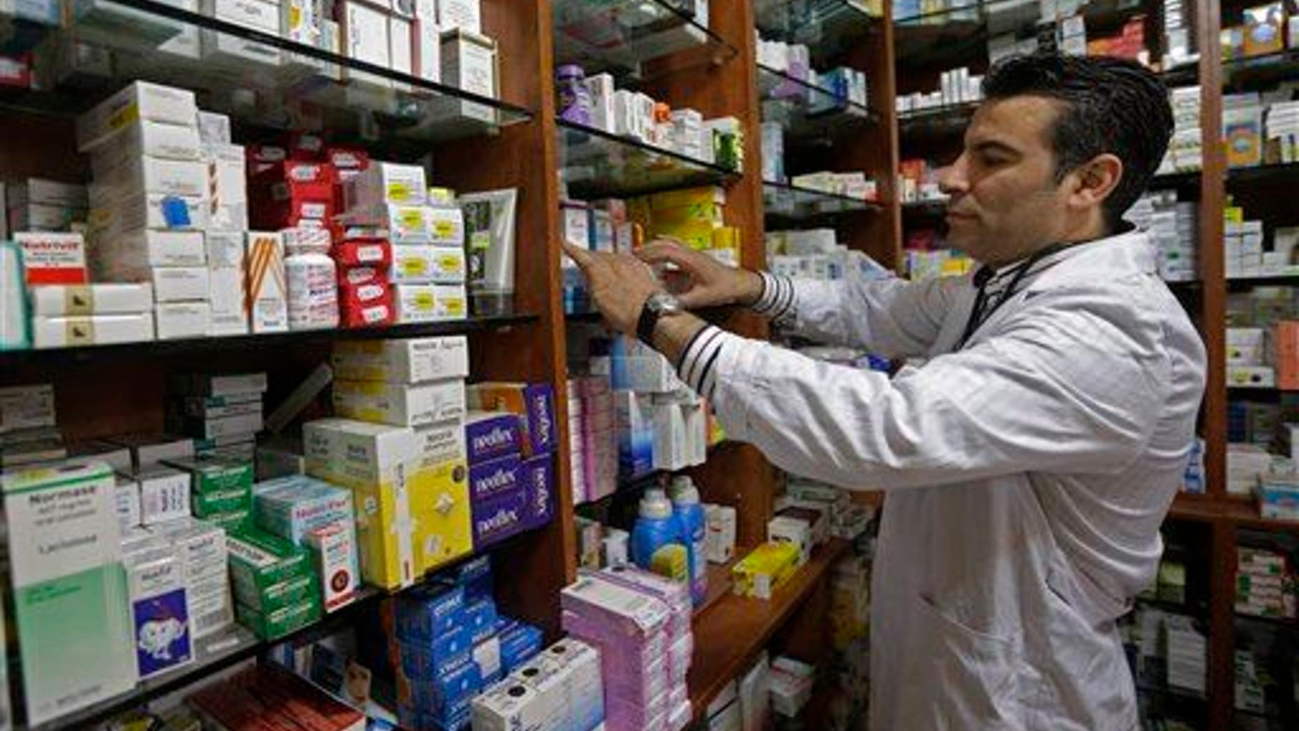 A pharmacist looks for medicine on a shelf at his pharmacy.