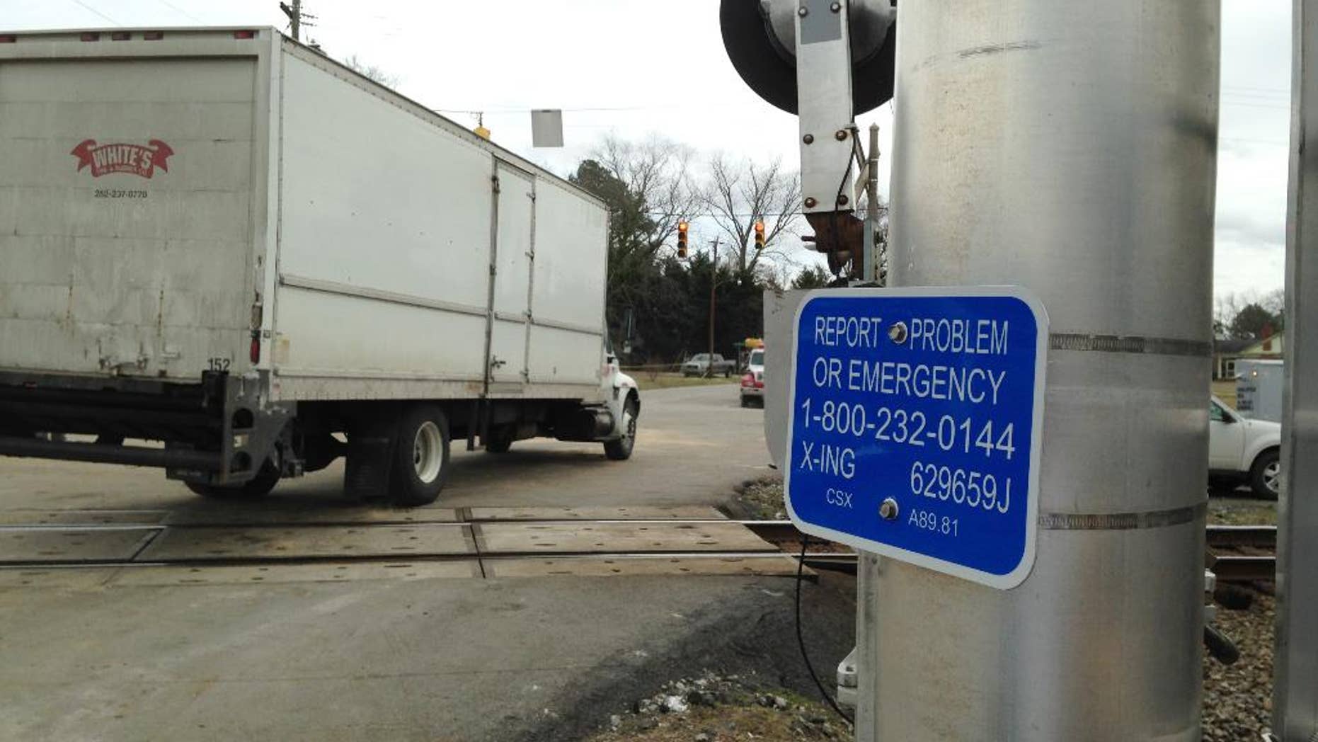 A truck passes over the train tracks near a sign listing an emergency number for railroad problems on Tuesday, March 10, 2015, in Halifax, N.C. A train collided with a truck, Monday injuring 55 people. The truck with a state trooper escort become stuck in the crossing but no calls were made to Amtrak about the problem, even though the sign should have been visible to the truck driver. (AP Photo /Jonathan Drew)