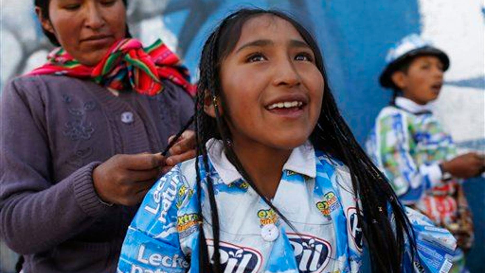 An indigenous woman braids her daughter's hair before the start of a parade in El Alto, Bolivia, Friday, Oct. 23, 2015.