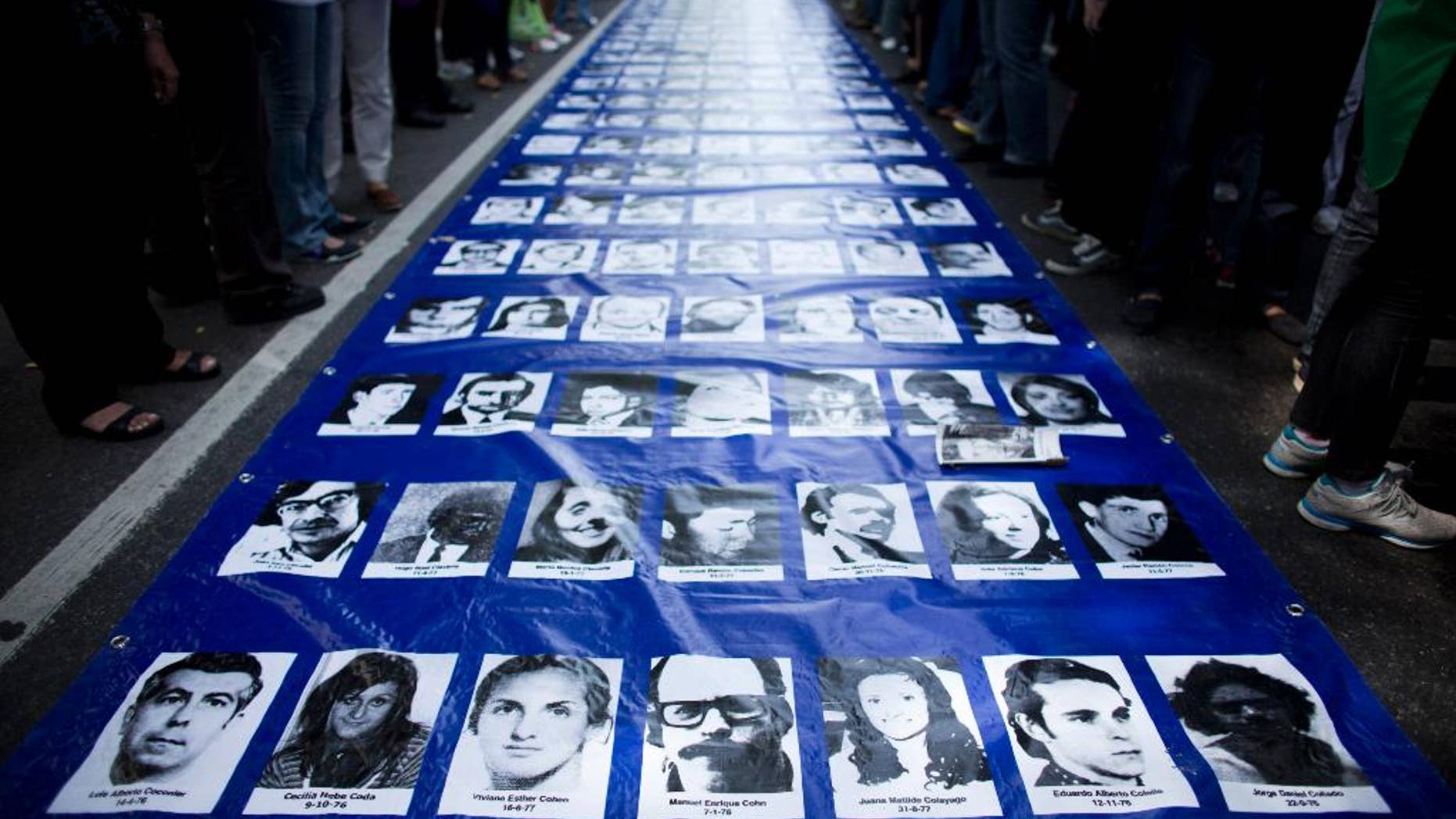 FILE - In this March 24, 2014 file photo, a banner filled with photos of people who went missing during the 1976-83 dictatorship lays on the ground before the start of a march marking the 38th anniversary of the 1976 military coup in Buenos Aires, Argentina. Four men accused of crimes against humanity during Argentina's dictatorship have decided to break a pact of silence among ex-members of the military who are on trial and collaborate with authorities in identifying victims and burial sites, a judge said Wednesday, Dec. 10, 2014. Human rights groups say about 30,000 people died or disappeared in Argentina's brutal dictatorship. (AP Photo/Victor R. Caivano, File)
