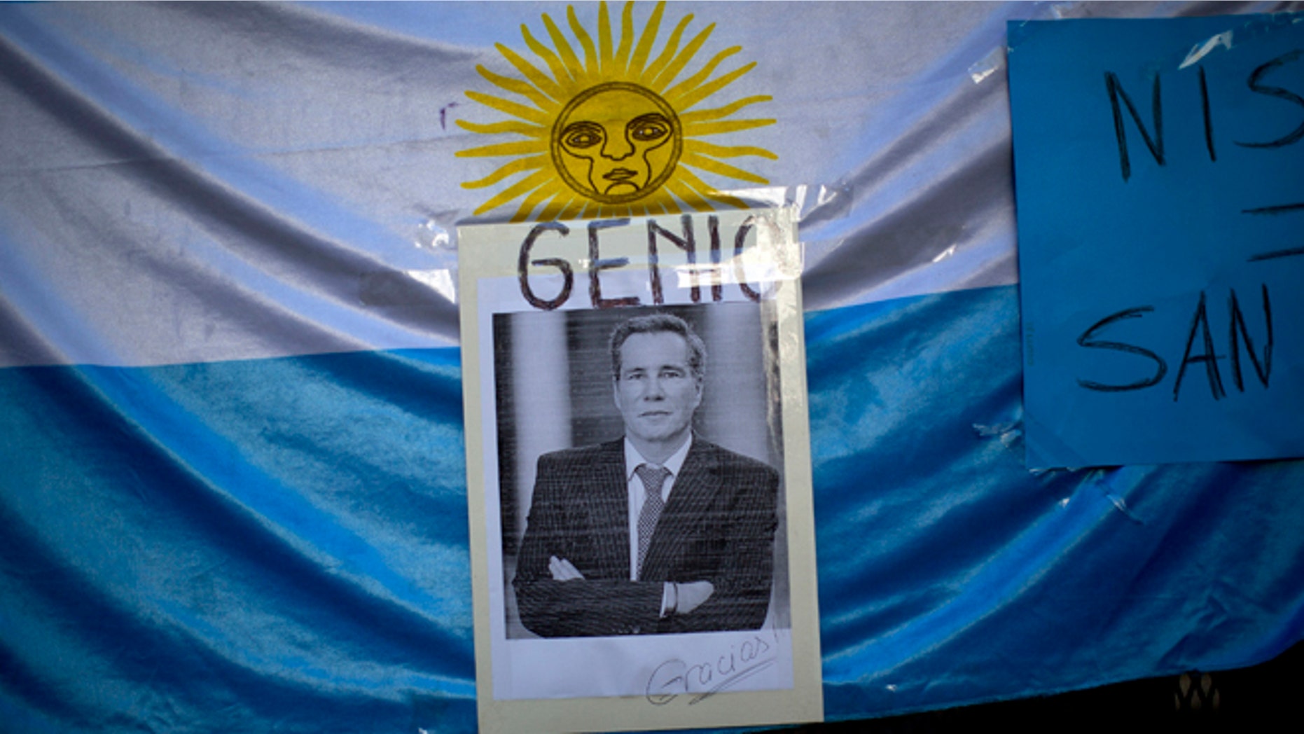A portrait of late prosecutor Alberto Nisman is seen pasted on an Argentine flag with a title that reads in Spanish "Genius," outside a funeral home during his wake in Buenos Aires, Argentina, Thursday, Jan. 29, 2015. Nisman was scheduled to appear before congress the day after he was found dead in his apartment on Jan. 18, to detail his allegations that President Cristina Fernandez had conspired to protect some of the Iranian suspects in the 1994 bombing of a Jewish center. The man who gave Nisman the gun that killed him said Wednesday that Nisman feared for the safety of his daughters and didn't trust the policemen protecting him. (AP Photo/Rodrigo Abd)