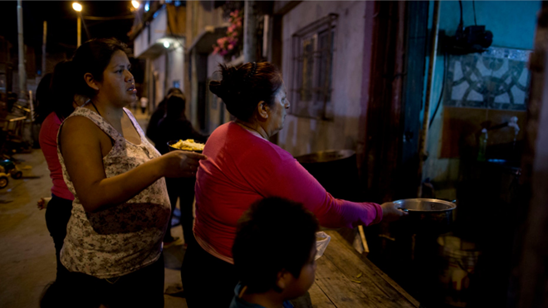 In this Oct. 13, 2016, women line up for a free dinner to take home to their families, from Norma Colque's soup kitchen in the Villa 31 neighborhood of Buenos Aires, Argentina. With the economy expected to shrink by 1.5 percent this year, President Mauricio Macri now admits his poverty goal isn't possible, and discontent is growing. (AP Photo/Natacha Pisarenko)