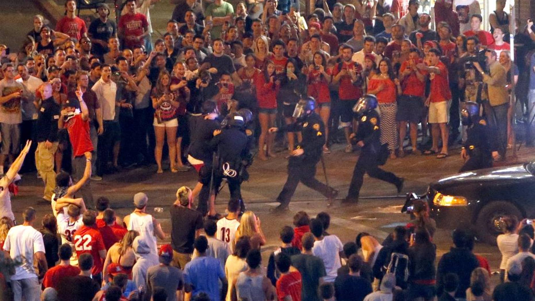 Tucson Police Officers rush out of their line to take a man into custody who had been taunting them and riling up a crowd of fans in Maingate Square, Saturday, March 29, 2014, in Tucson Ariz. following Arizona's loss to Wisconsin 64-63 in the West Region NCAA final. (AP Photo/Arizona Daily Star, Kelly Presnell)