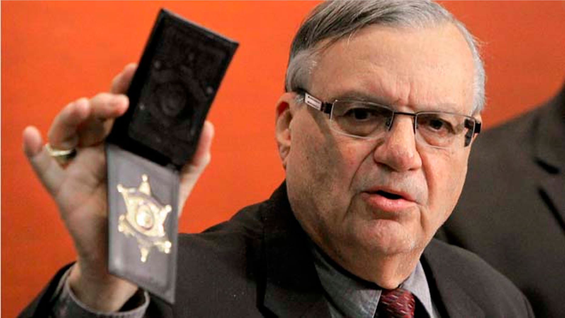 FILE- In this Dec. 21, 2011 file photo, Maricopa County Sheriff Joe Arpaio shows his badge as he holds a ceremony where 92 of his immigration jail officers, who lost their federal power to check whether inmates are in the county illegally, turn in their credentials after federal officials pulled the Sheriff's office immigration enforcement powers in Phoenix. The U.S. Justice Department is putting Arpaio on trial next month in a civil rights case that will focus in part on how the sheriff investigated and criminally charged people who crossed him from 2007 until 2010. (AP Photo/Ross D. Franklin, File)