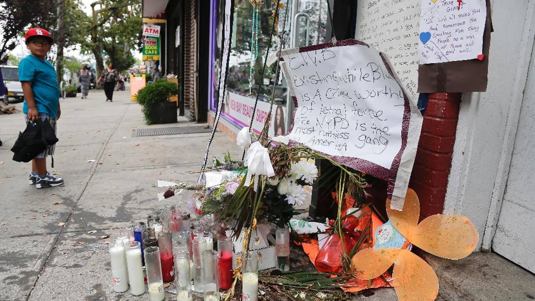 August 1, 2014: A young boy stops as he passes a makeshift memorial for Eric Garner in the Staten Island borough of New York. Garner was put in a chokehold while being arrested at the site last month for selling untaxed loose cigarettes. On Friday, the medical examiner ruled Garner's death to be a homicide caused by a police chokehold. (AP Photo/Julie Jacobson)